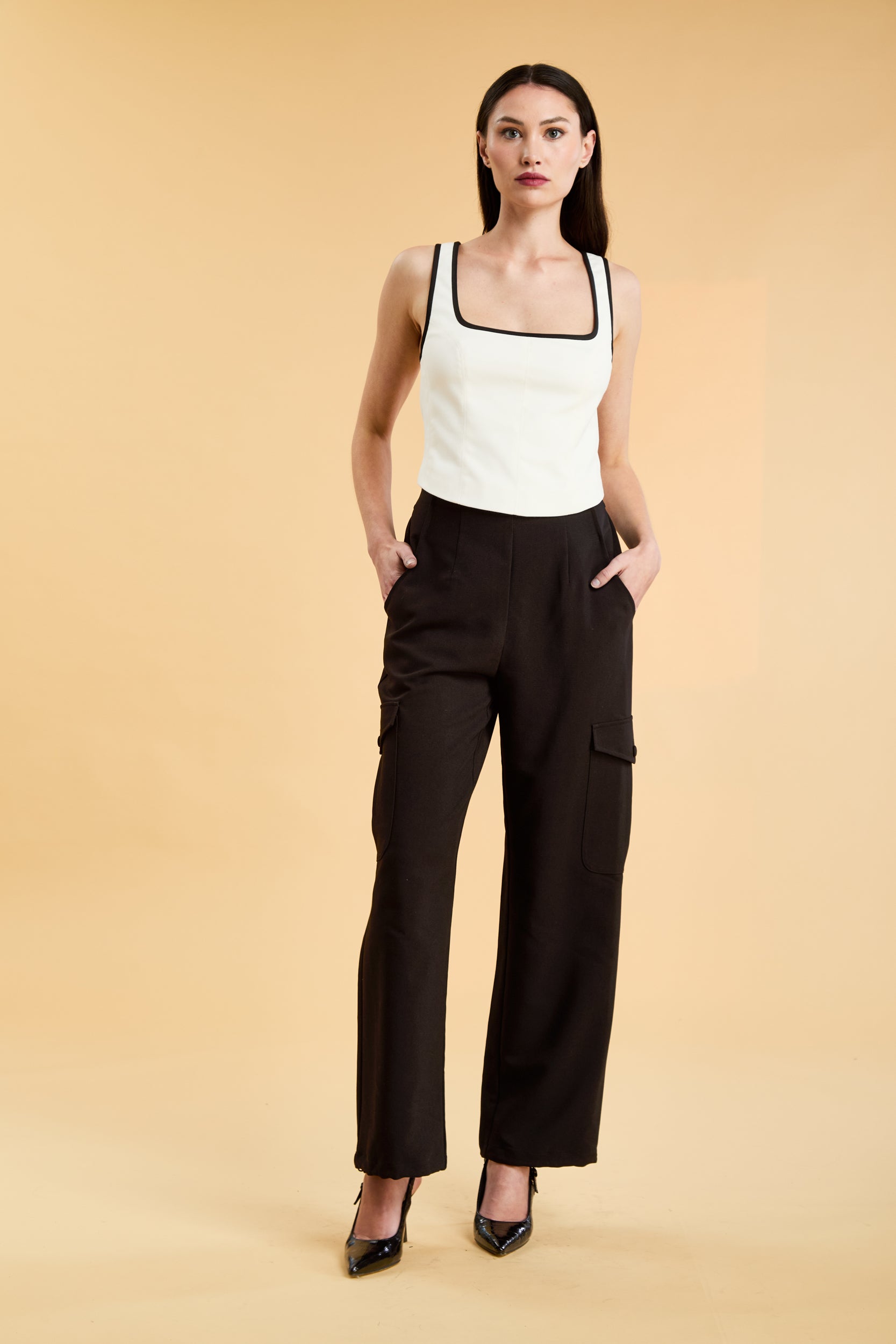 Person wearing a White Triplicity Eloise sleeveless tank top and Black Adelaide pants on a beige background front view full body