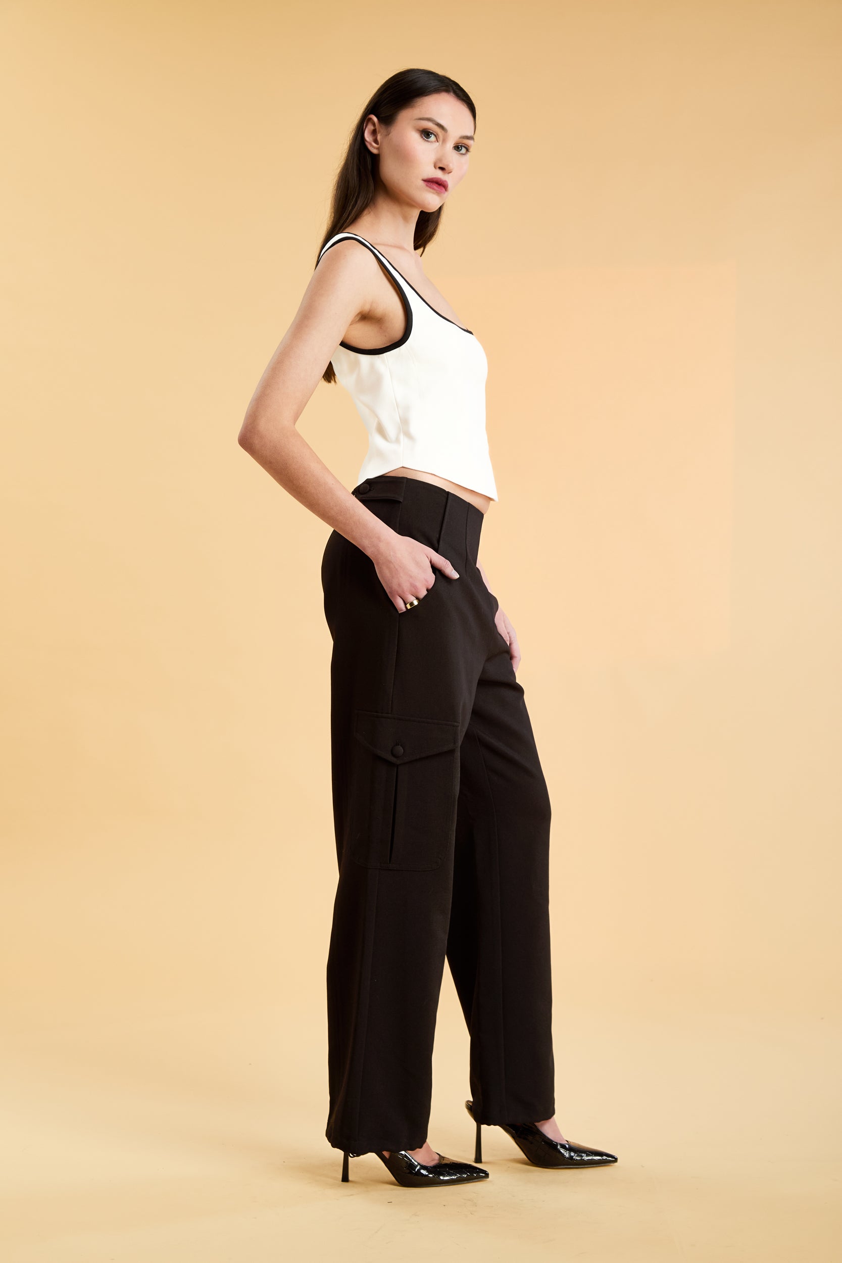 Person wearing a White Triplicity Eloise sleeveless tank top and Black Adelaide pants on a beige background three quarter view full body