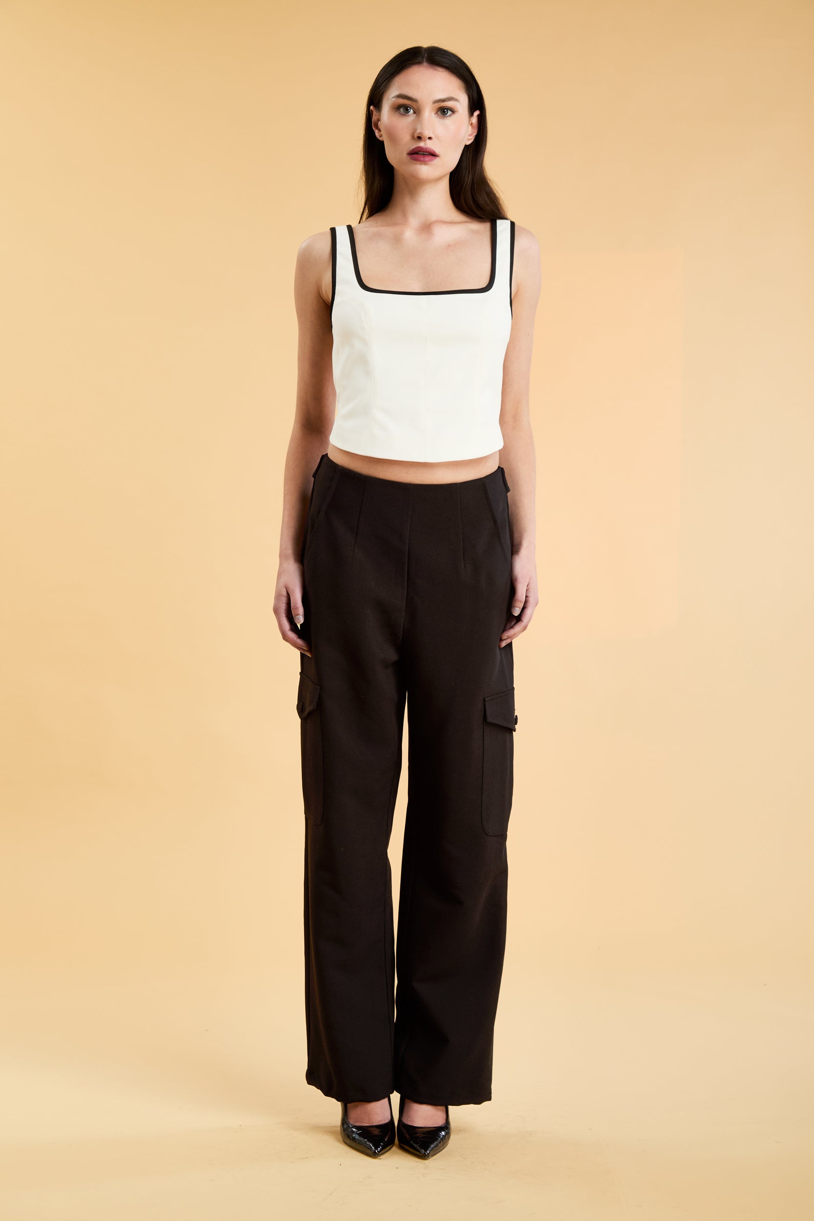 Person wearing a White Triplicity Eloise sleeveless tank top and Black Adelaide pants on a beige background front view full body