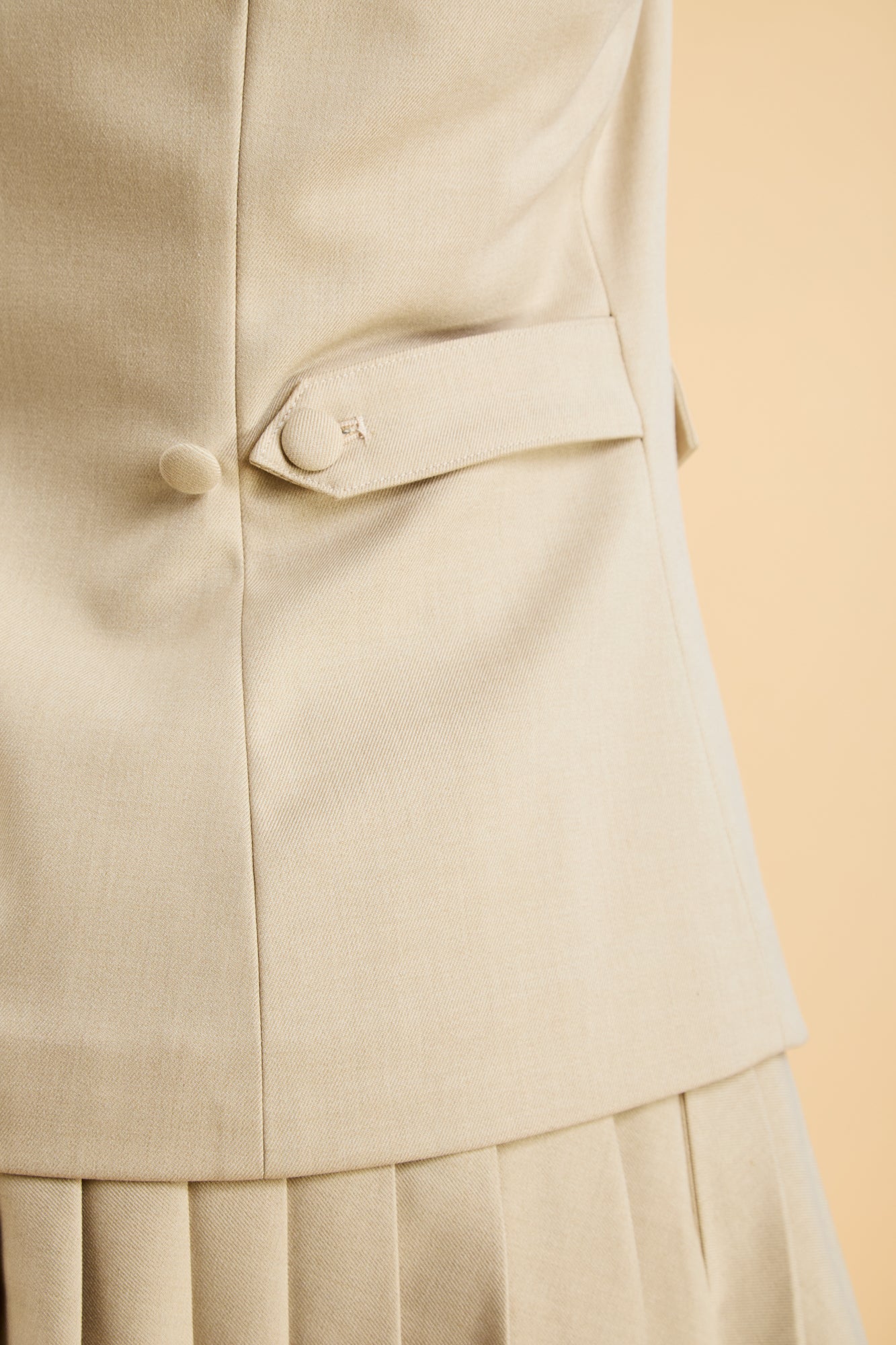 Close-up of a Oat colored Triplicity Vest top with buttons and pleated skirt.