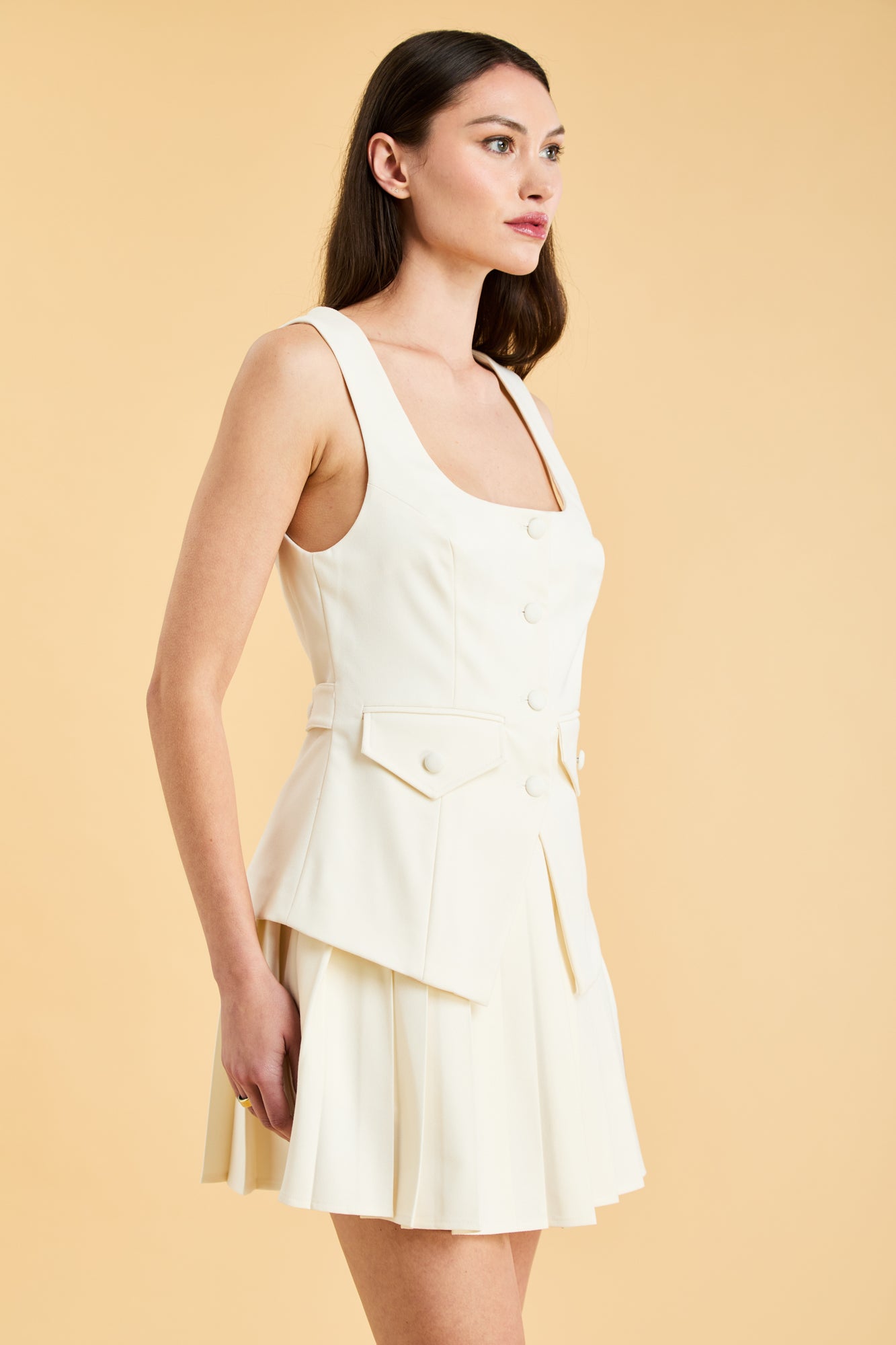 Woman wearing a White Triplicity Georgiana vest top on a Triplicity White pleated midi skirt against a beige background three quarter view close up
