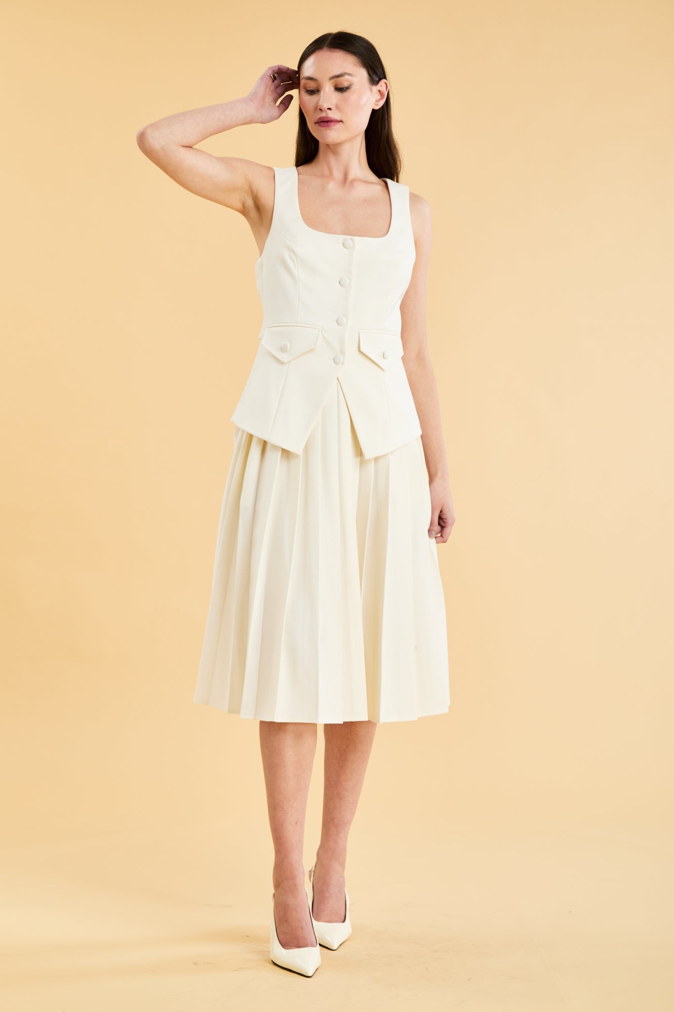 Woman wearing a White Triplicity Georgiana vest top on a Triplicity White pleated midi skirt against a beige background front view full body