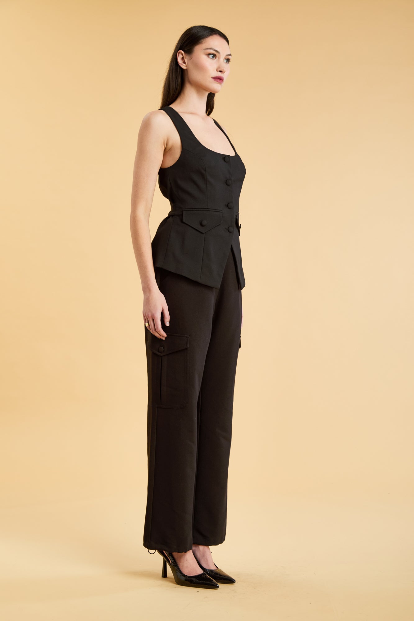 Woman wearing a Black Triplicity Georgiana Vest top on the Triplicity Triplicity Adelaide cargo pant on a beige background three quarter view full body