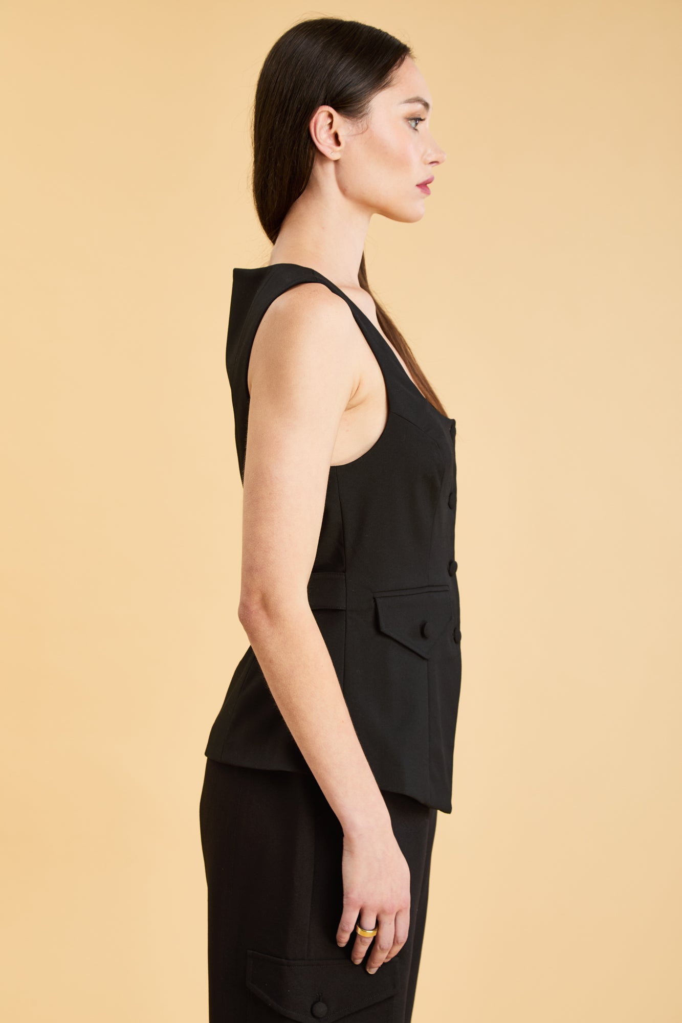 Woman wearing a Black Triplicity Georgiana Vest top on the Triplicity Triplicity Adelaide cargo pant on a beige background side view close up