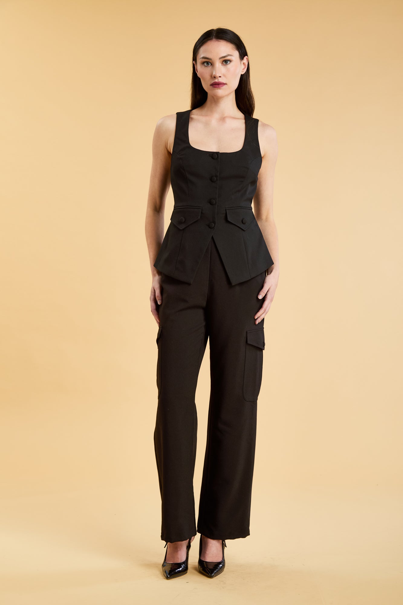 Woman wearing a Black Triplicity Georgiana Vest top on the Triplicity Triplicity Adelaide cargo pant on a beige background front view full body