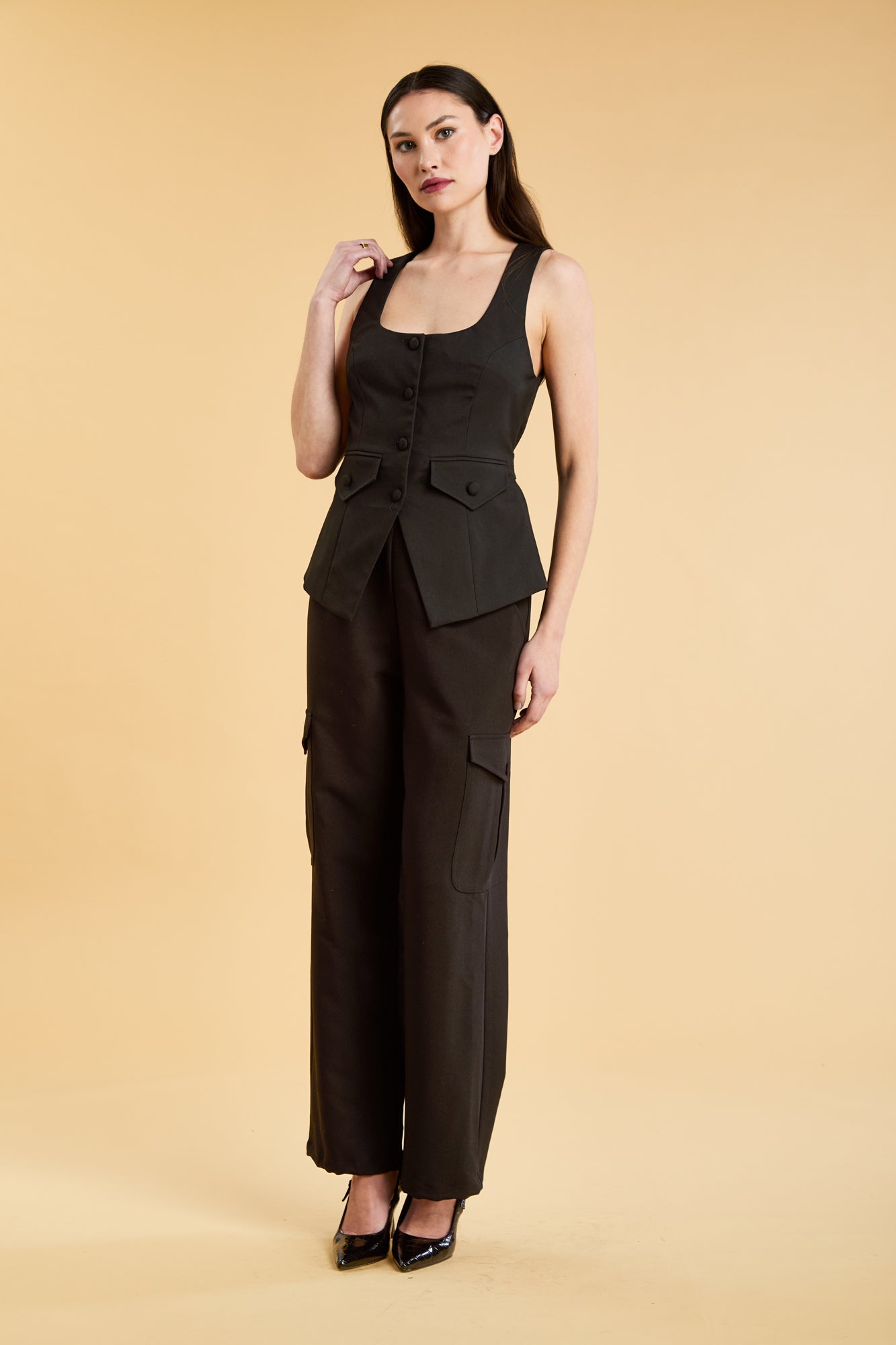 Woman wearing a Black Triplicity Georgiana Vest top on the Triplicity Triplicity Adelaide cargo pant on a beige background front view full body