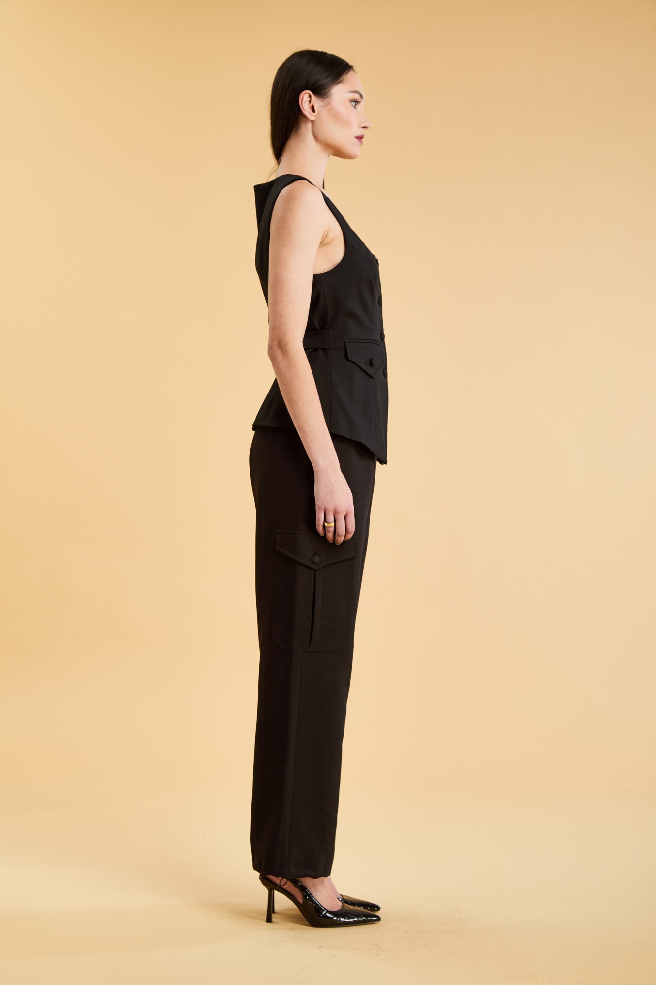 Woman wearing a Black Triplicity Georgiana Vest top on the Triplicity Triplicity Adelaide cargo pant on a beige background side view full body