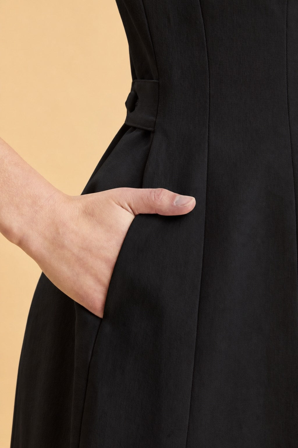 Close-up of a person wearing a black pink dress with her hand in her pocket and a yellow background