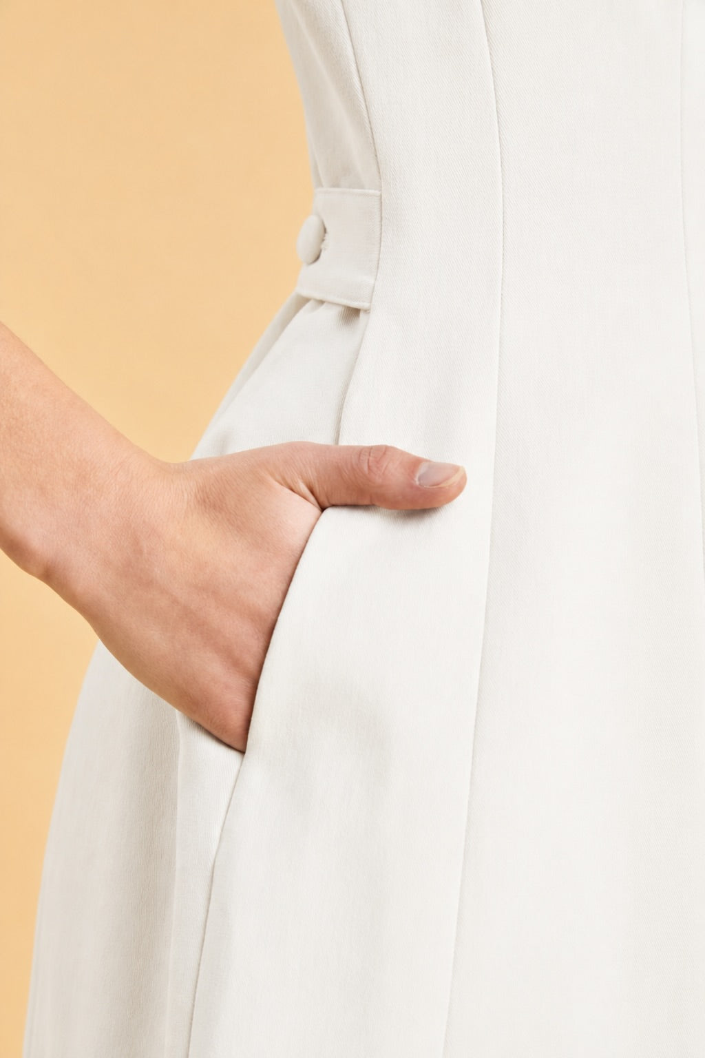 Close-up of a person wearing a blush pink dress with her hand in her pocket and a yellow background