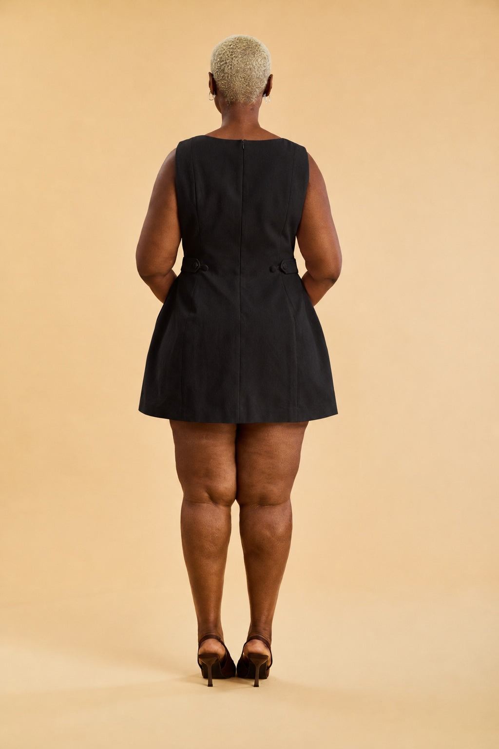 Person wearing a black sleeveless dress on a beige background