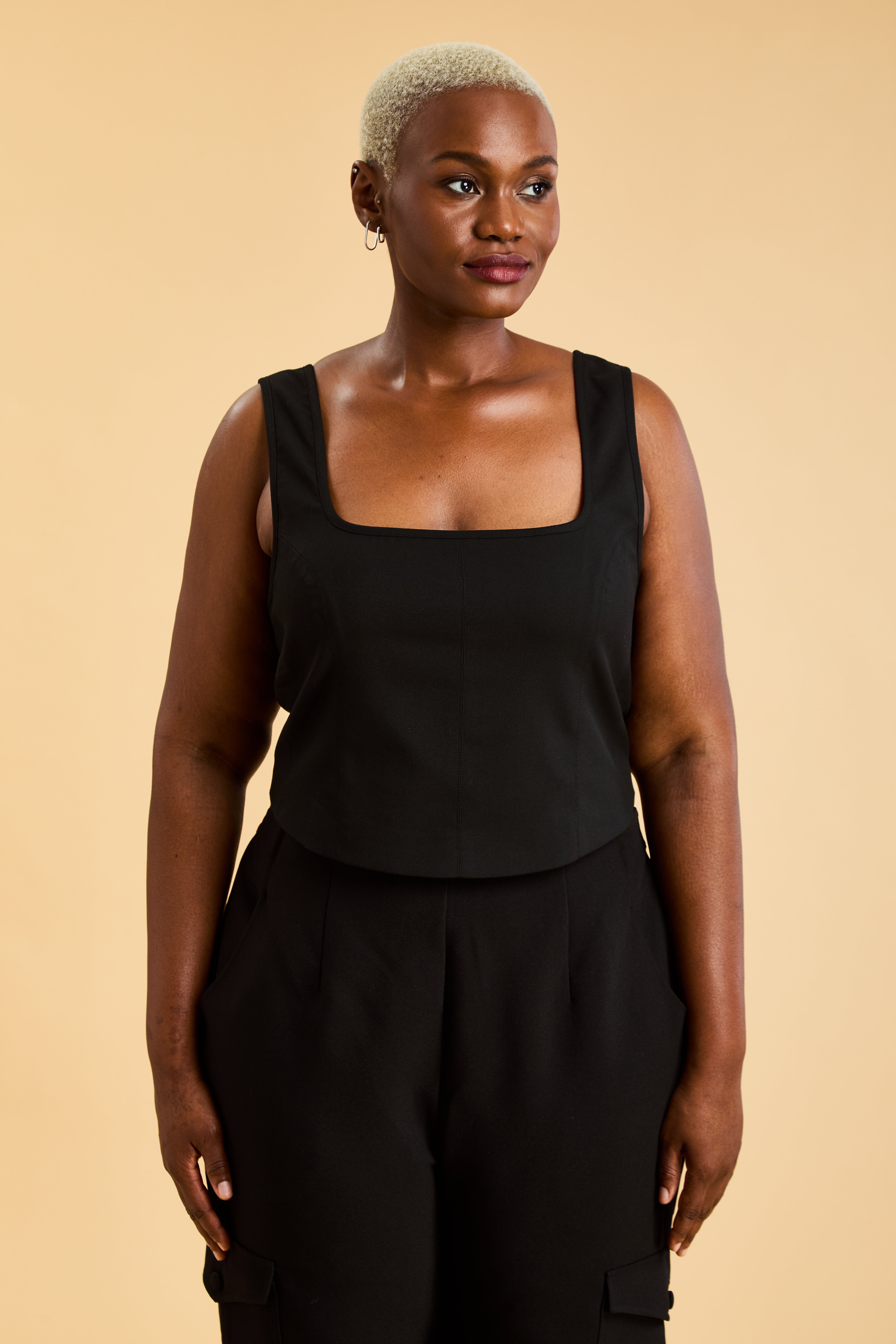 Woman wearing a Black Triplicity sleeveless Eloise tank up against a beige background front view close up