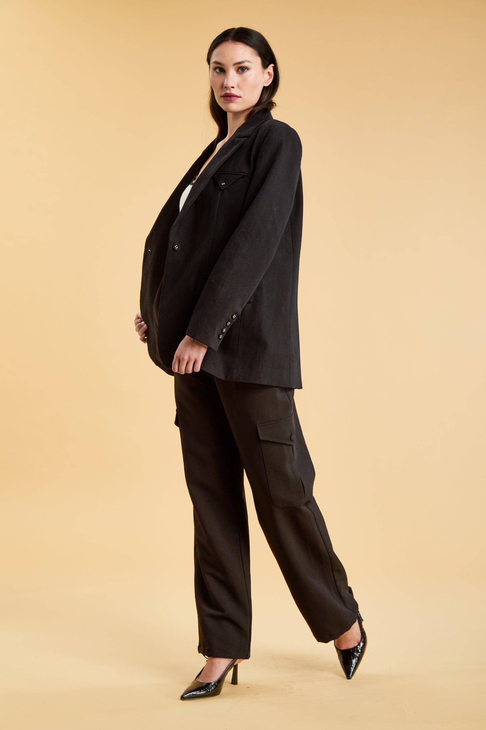 Woman wearing a Black oversized triplicity blazer over a white top on a beige background front view full body