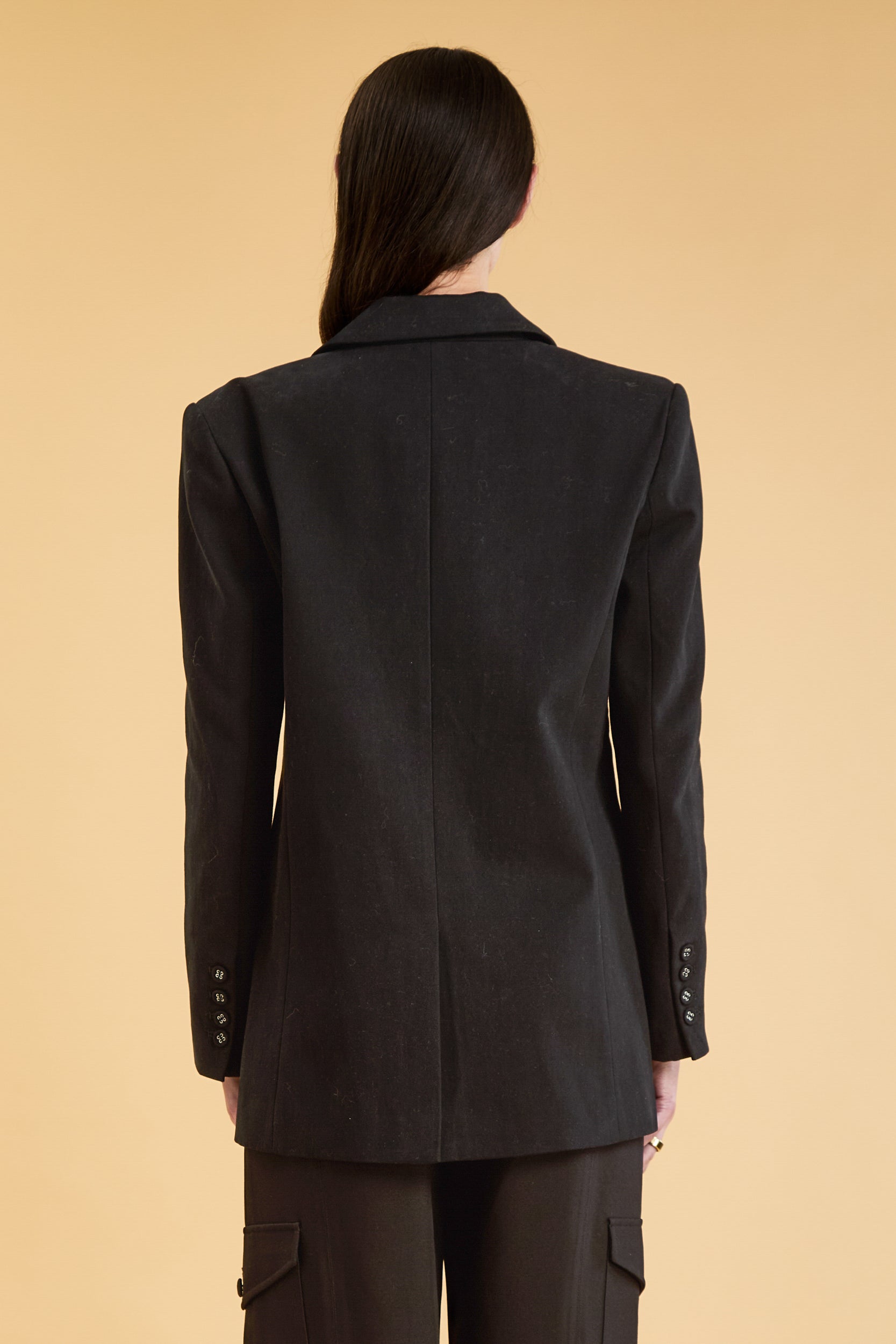 Woman wearing a Black oversized triplicity blazer over a white top on a beige background back view cropped
