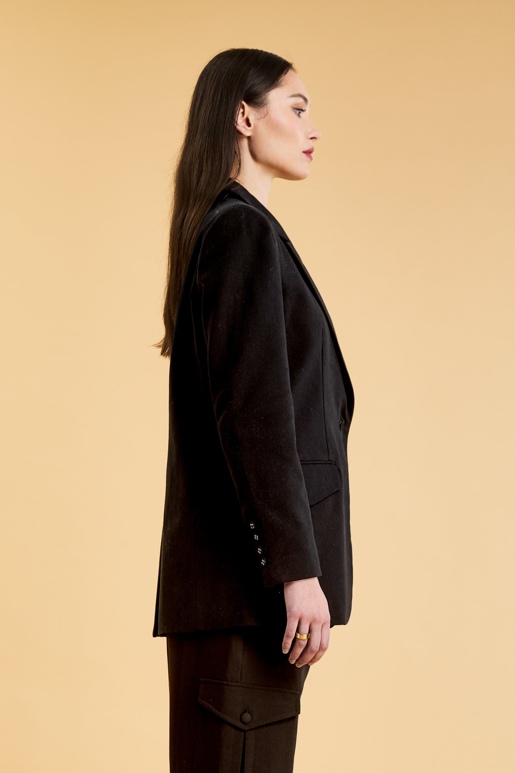 Woman wearing a Black oversized triplicity blazer over a white top on a beige background side view cropped
