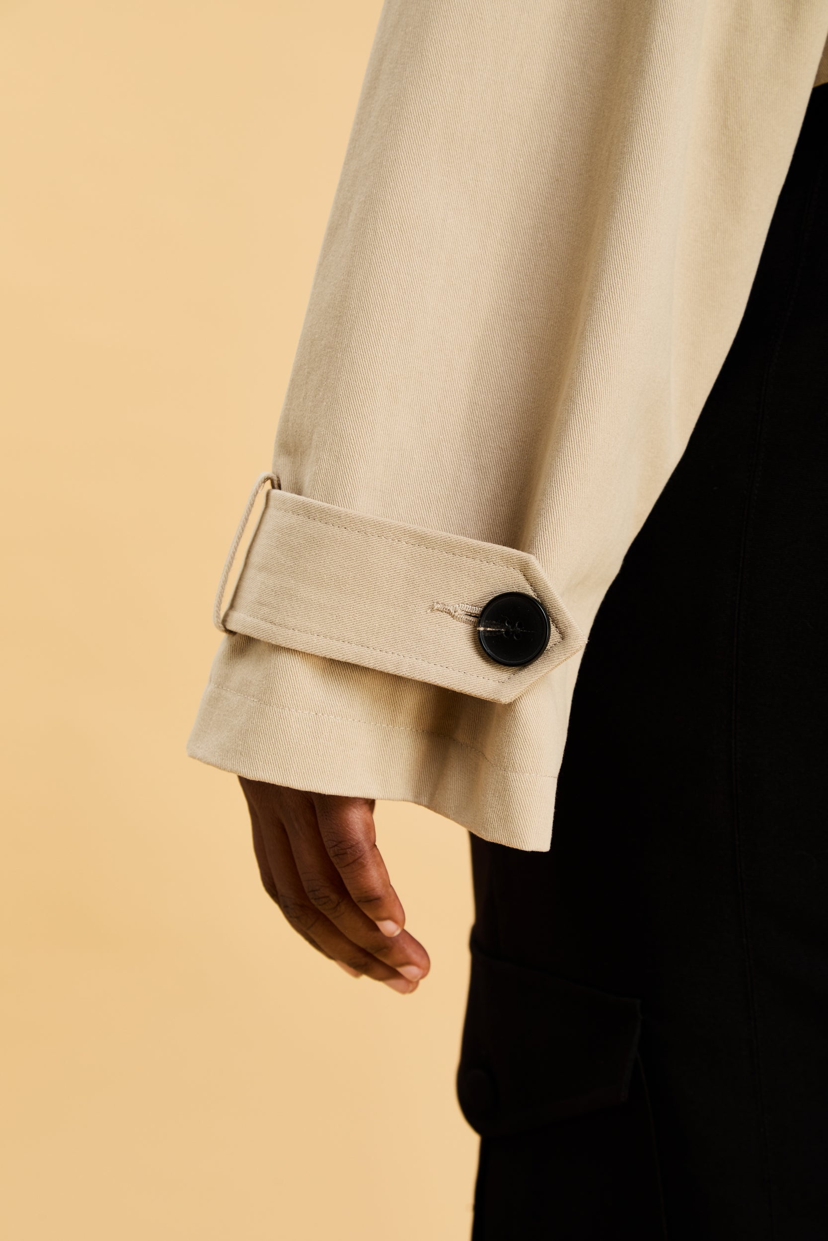 Close-up of a beige coat sleeve with a button on a beige background