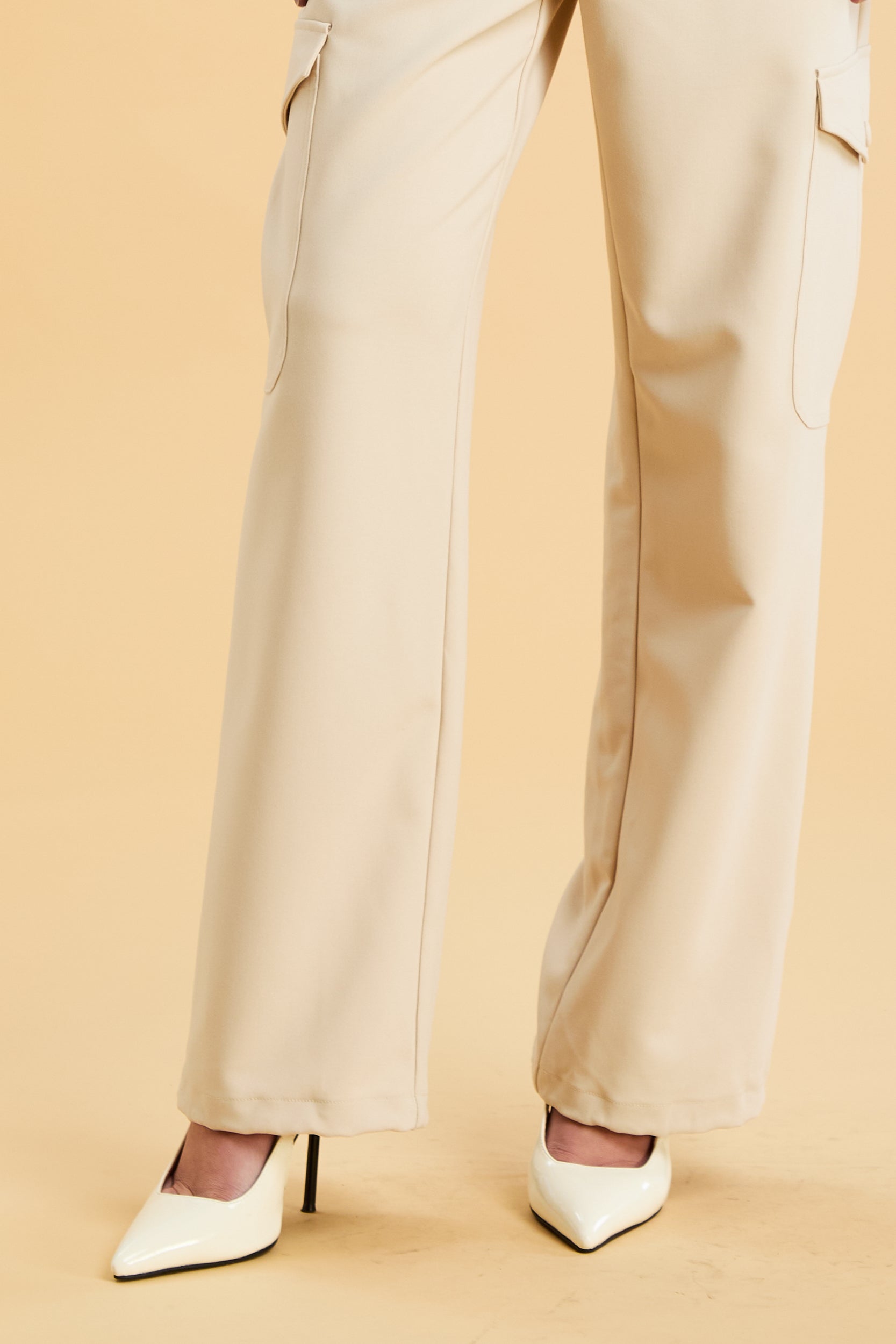 Woman wearing a white sleeveless double zipper top and beige almond Triplicity trousers cargo pants on a beige background
