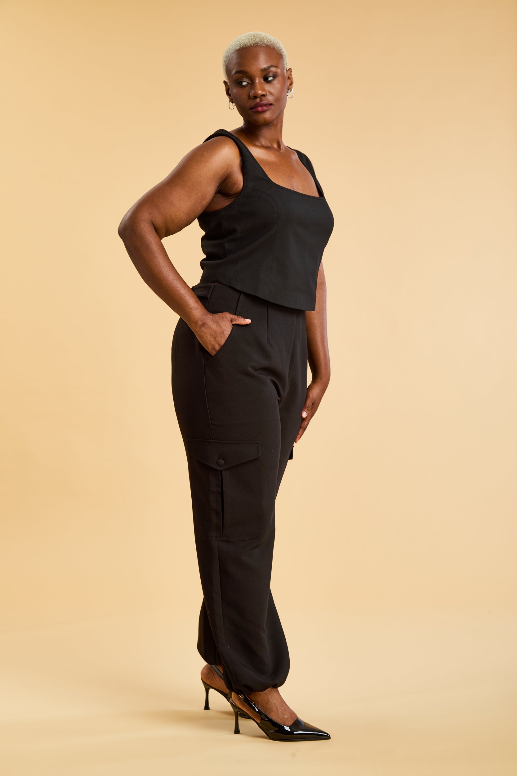 Woman wearing a black sleeveless top and pants against a beige background