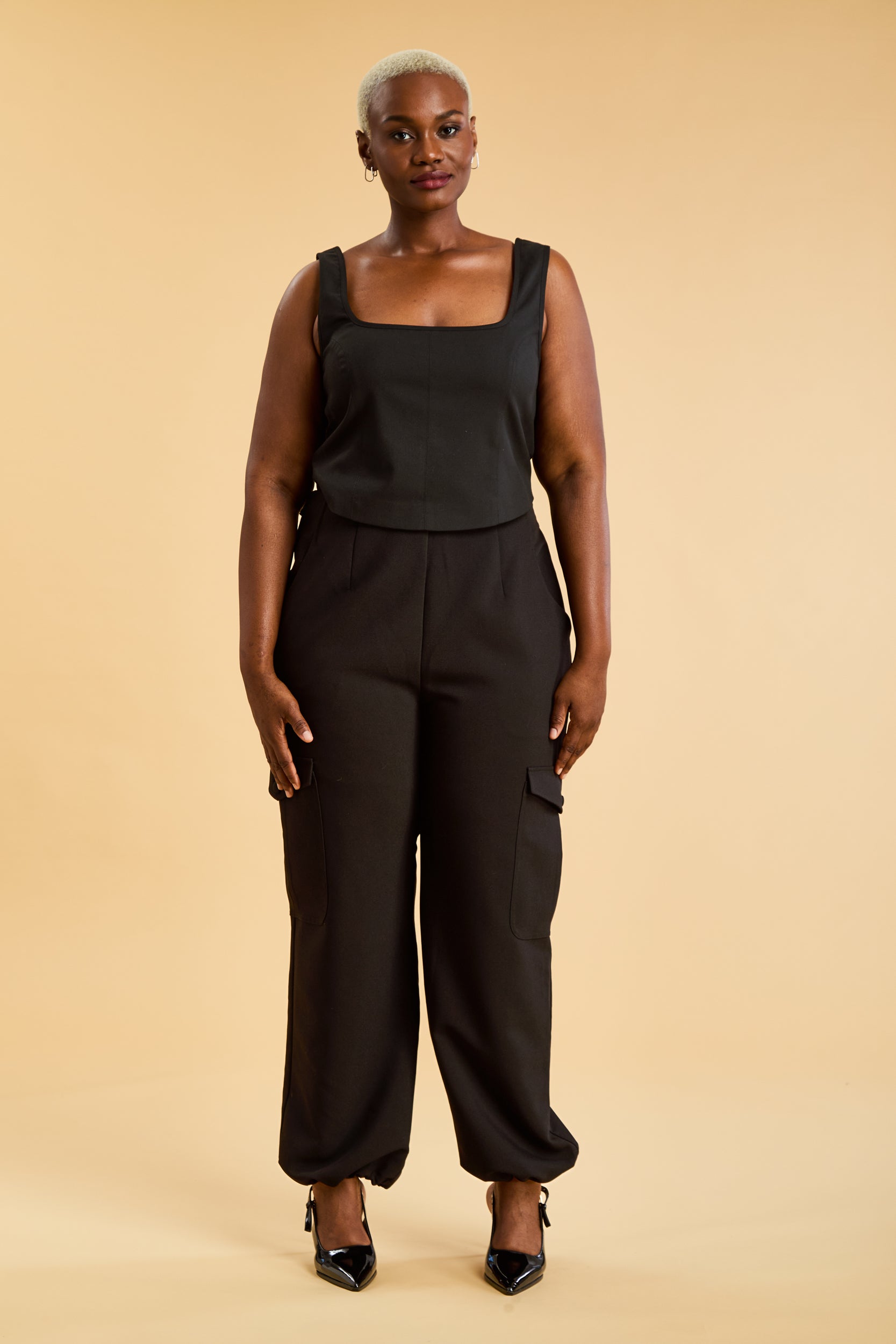 Woman wearing a black sleeveless top and wide-leg pants on a beige background