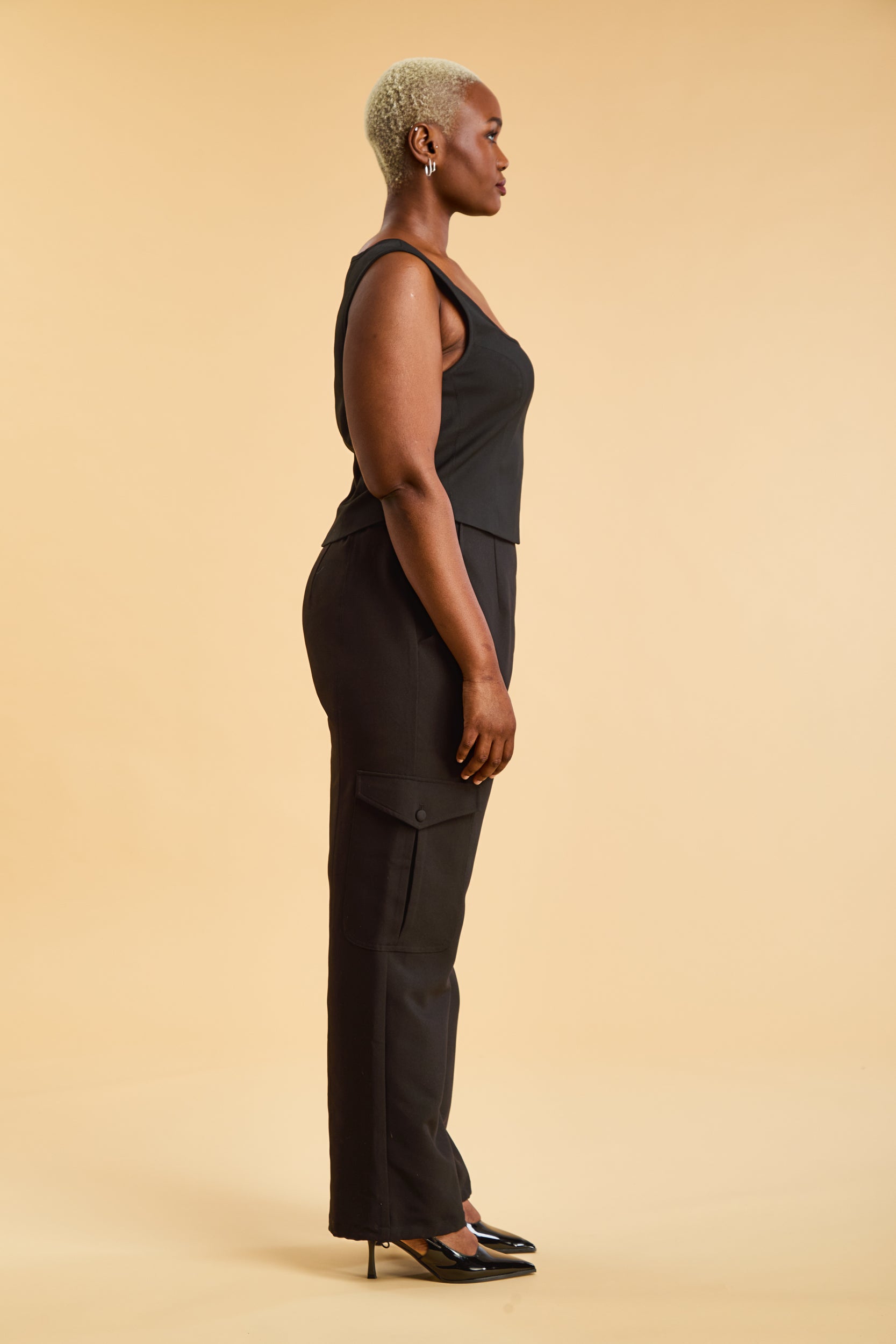 Woman wearing a black top and black cargo pants on a beige background