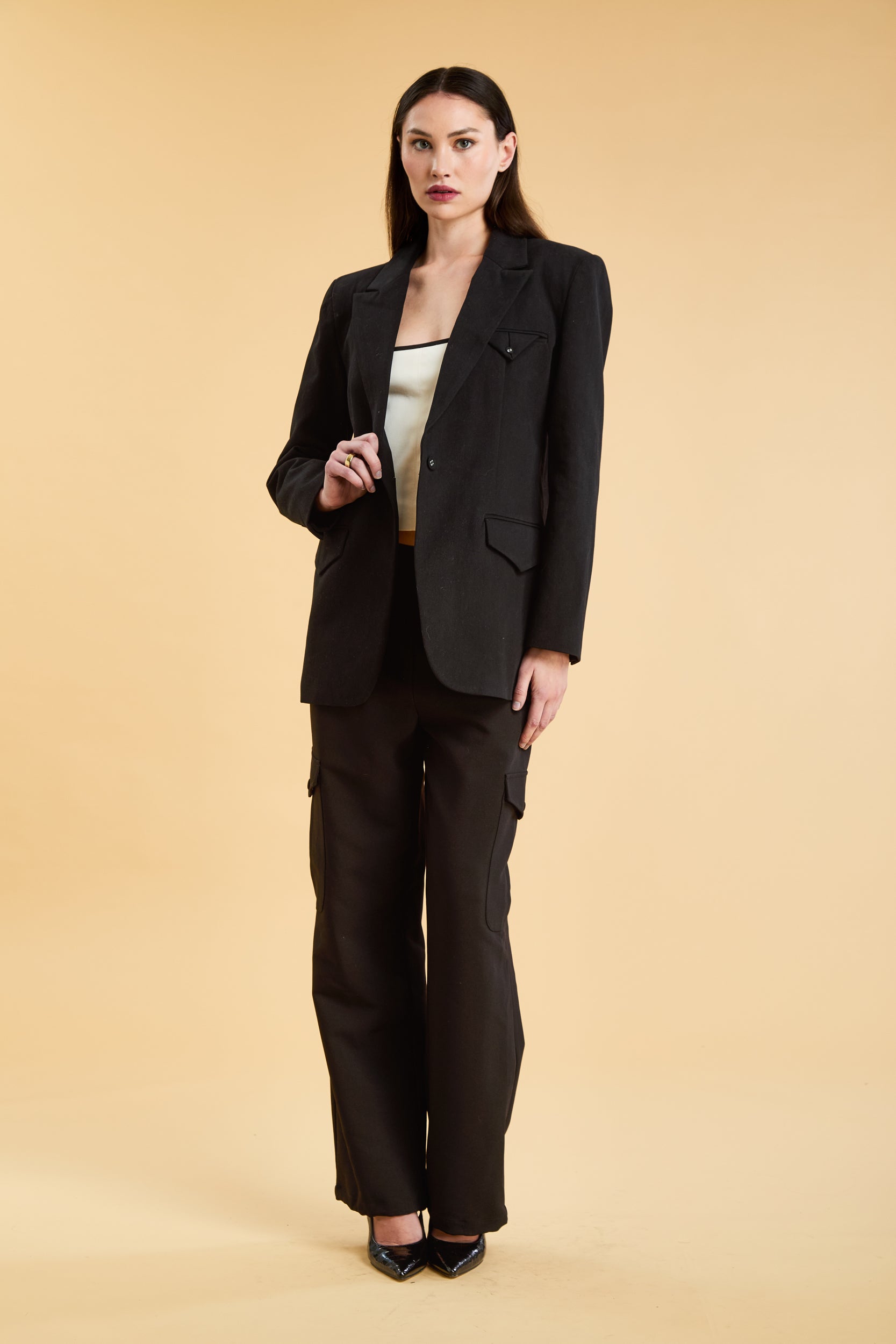 Woman wearing a black blazer and black cargo pants on a beige background
