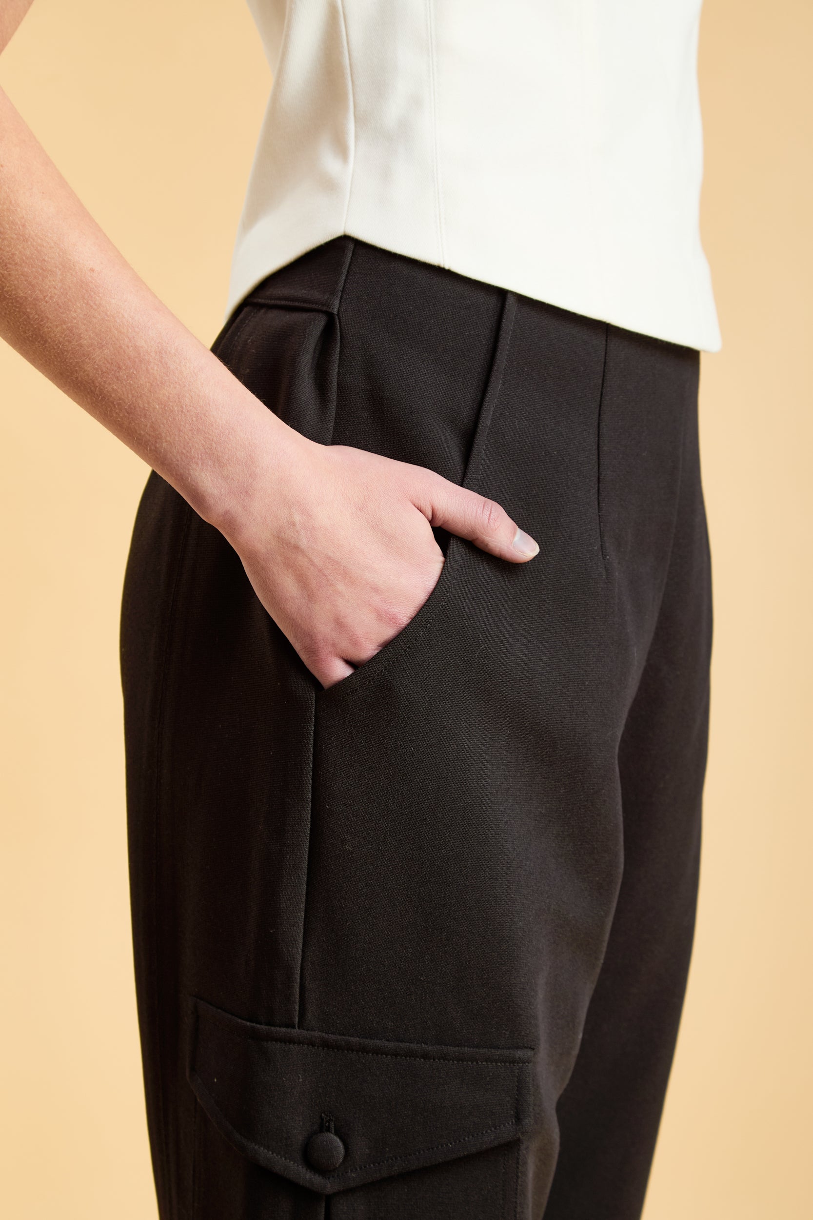 Woman wearing a white top and black cargo pants on a beige background