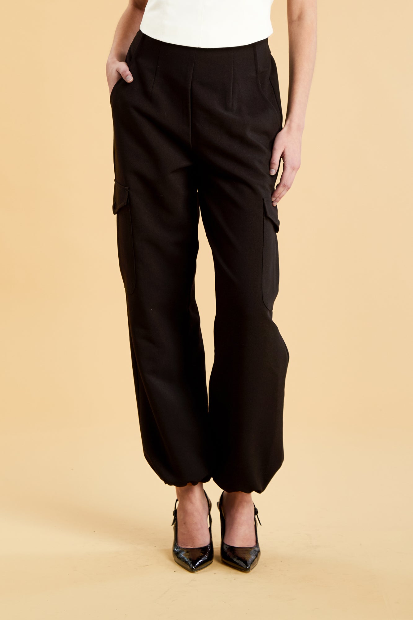 Woman wearing a white top and black cargo pants on a beige background