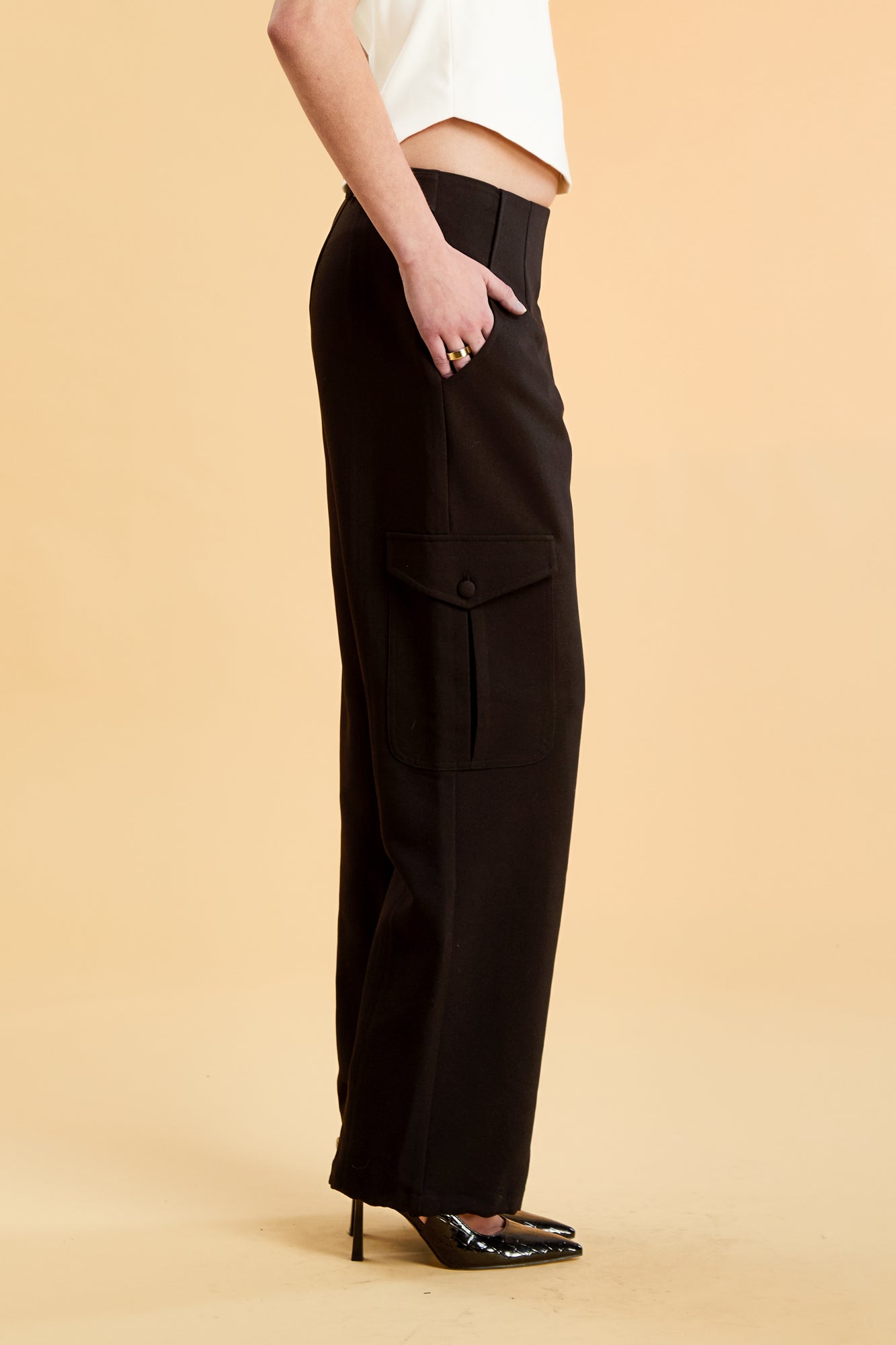 Woman wearing a white top and black cargo pants on a beige background