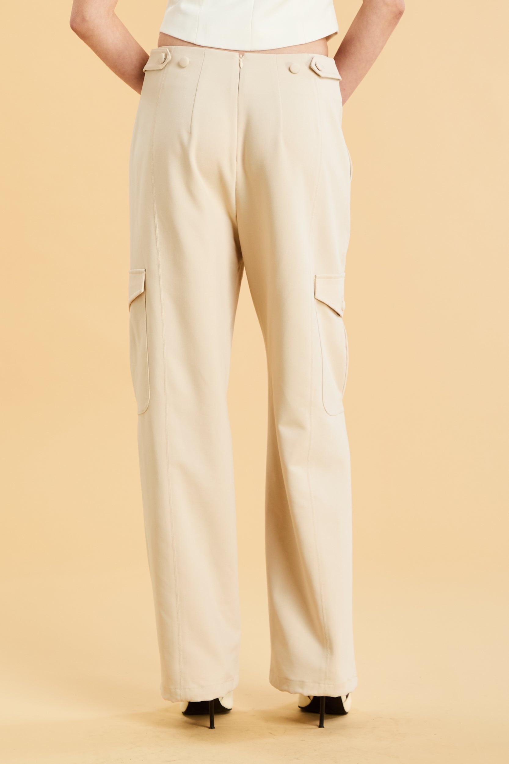 Woman wearing a white sleeveless double zipper top and beige almond Triplicity trousers cargo pants on a beige background