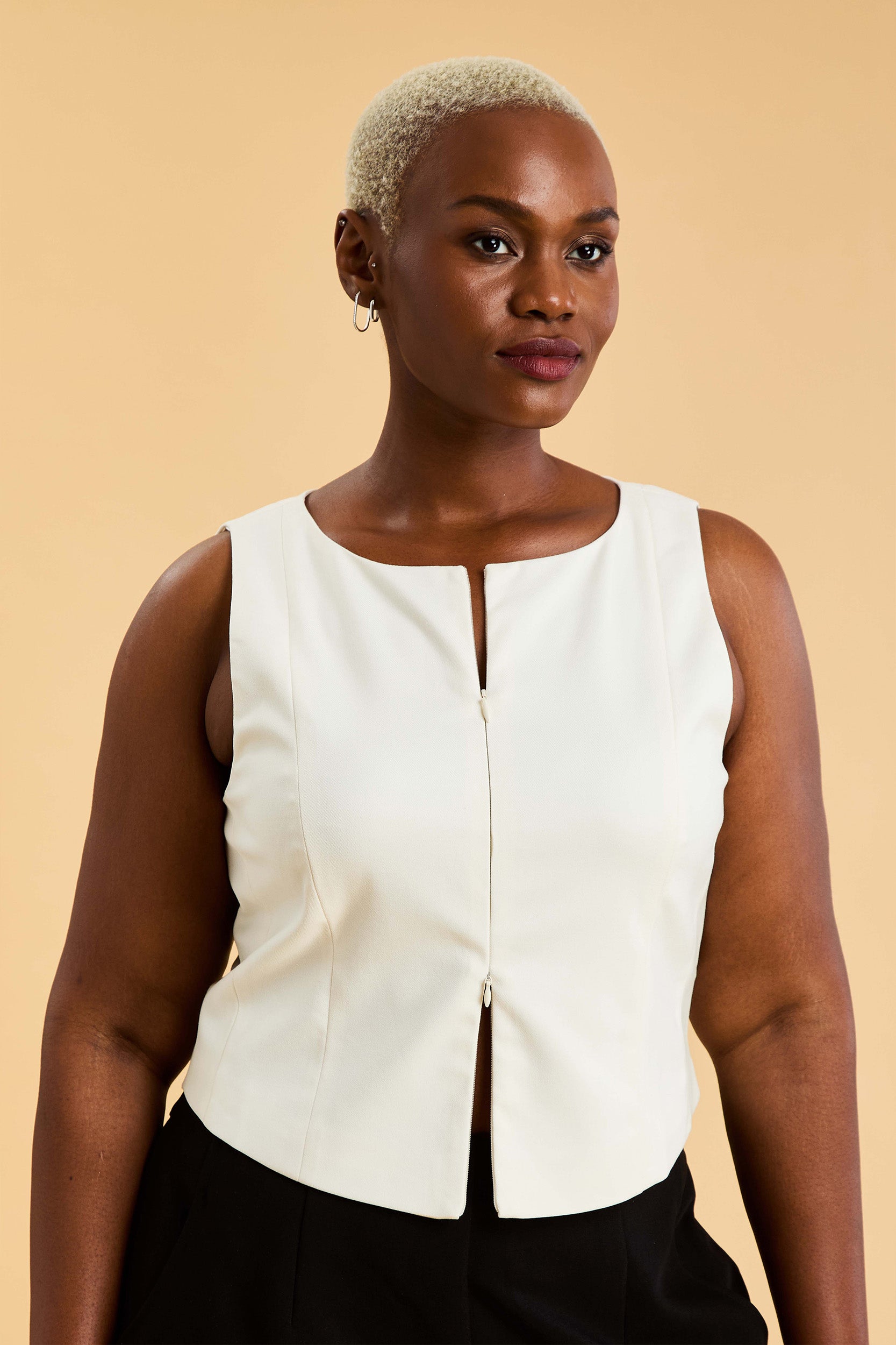 Woman wearing a white sleeveless top against a beige background