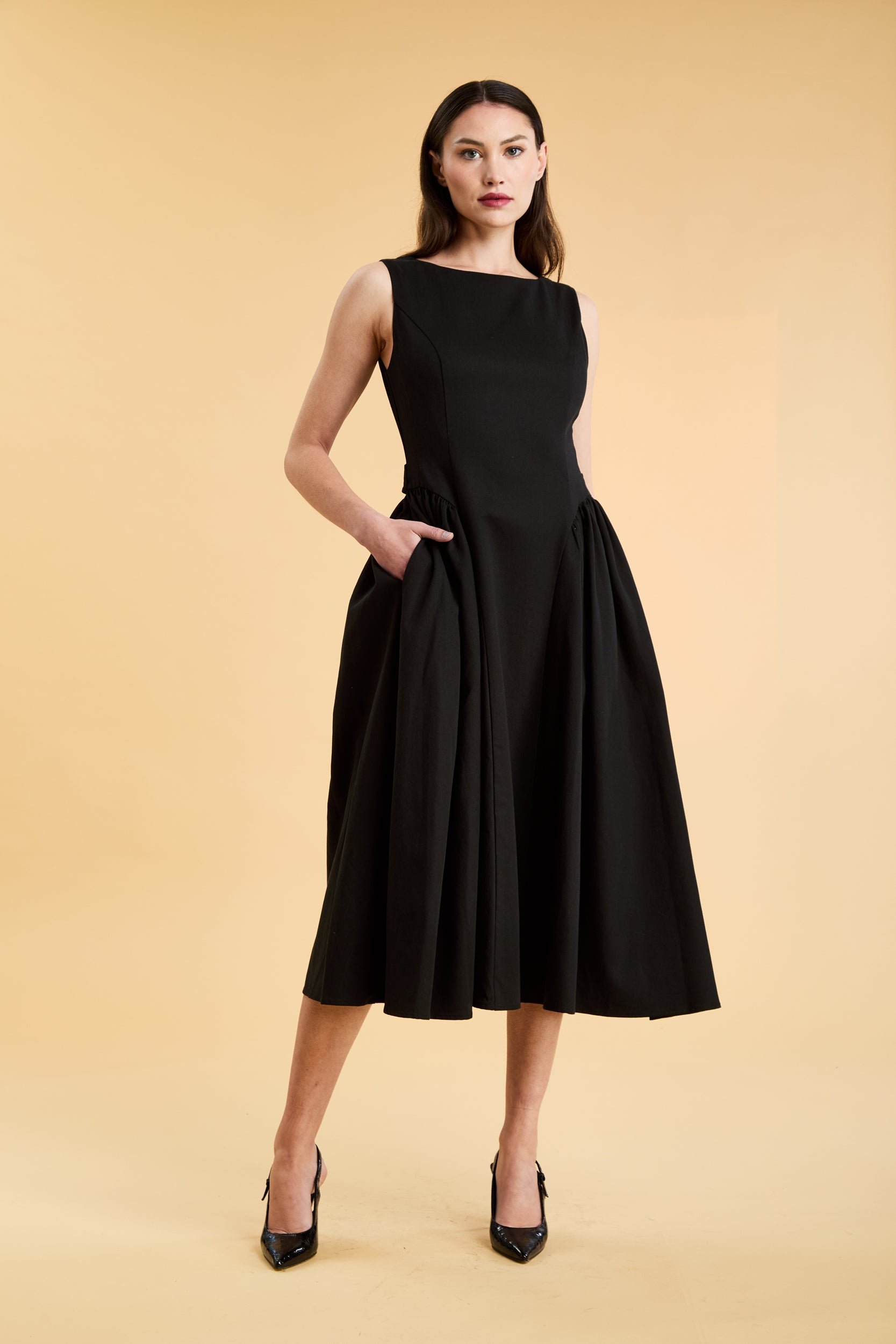 Woman wearing a Triplicity Black sleeveless midi dress with gathered side panels on a beige background