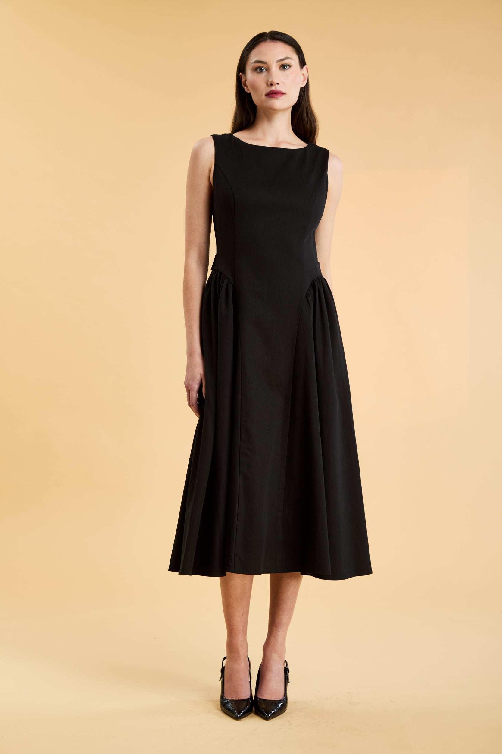 Woman wearing a Triplicity Black sleeveless midi dress with gathered side panels on a beige background