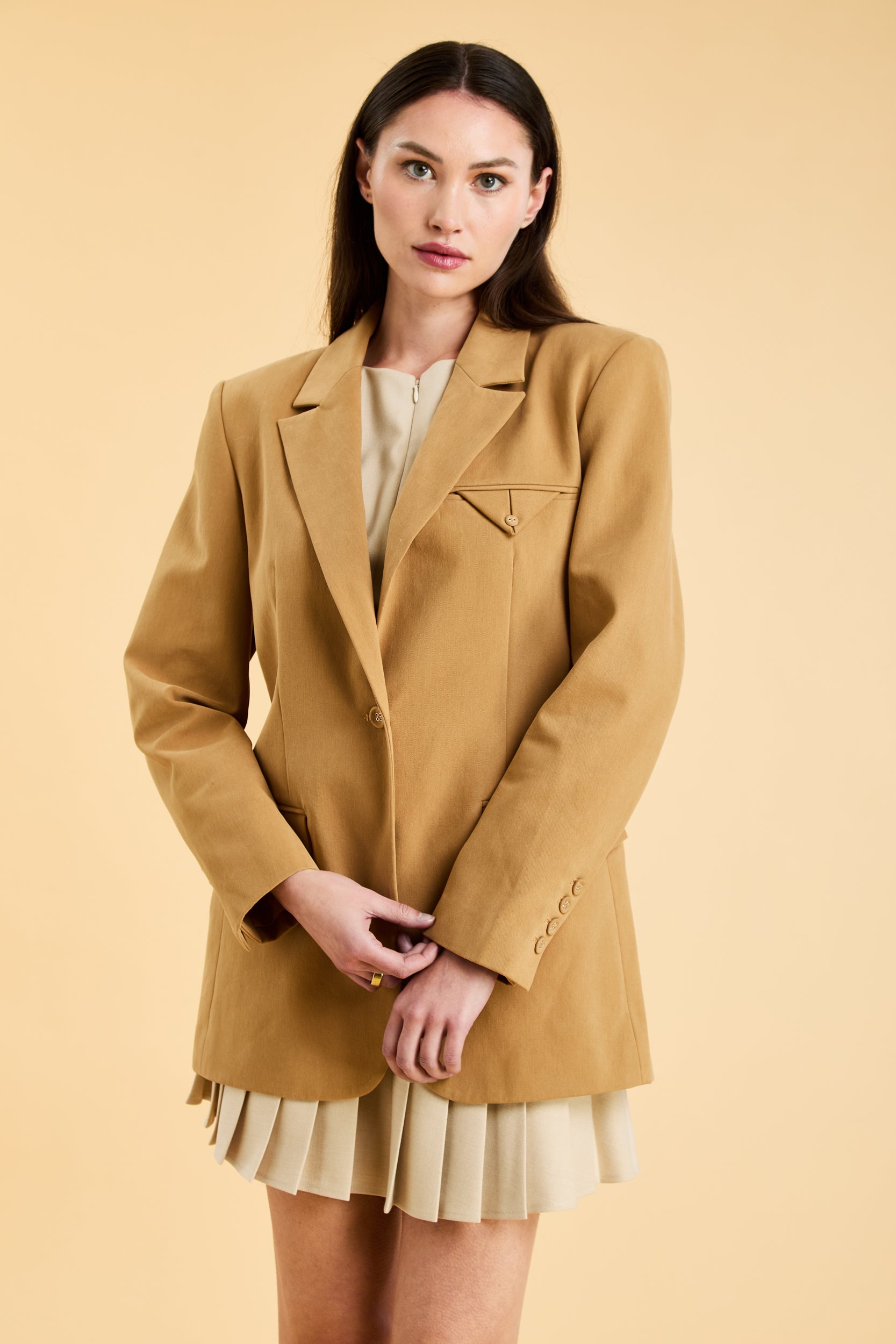 Woman wearing a Camel colored blazer over a light-colored dress on a beige background