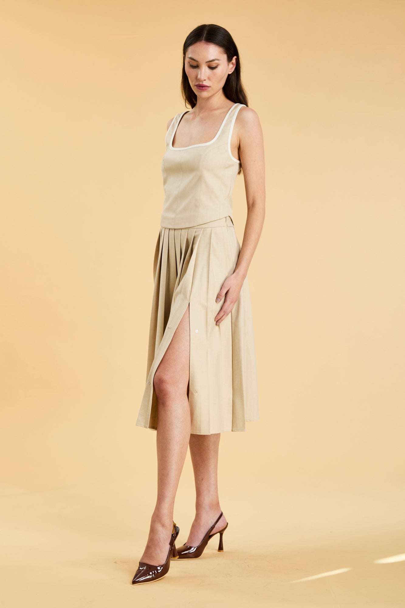 Woman wearing a beige sleeveless top and skirt on a yellow background