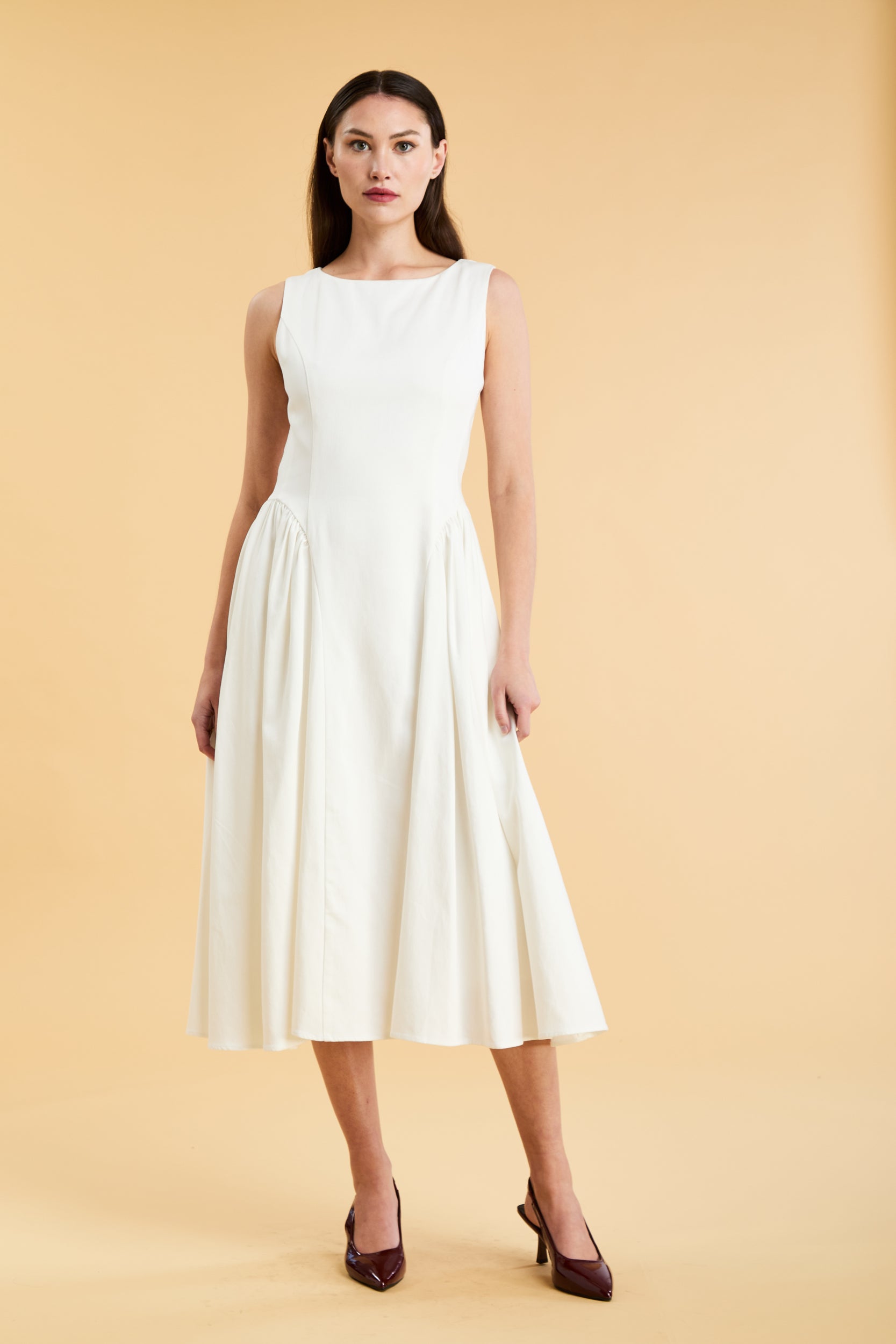 Woman wearing a Triplicity White sleeveless midi dress with gathered side panels on a beige background