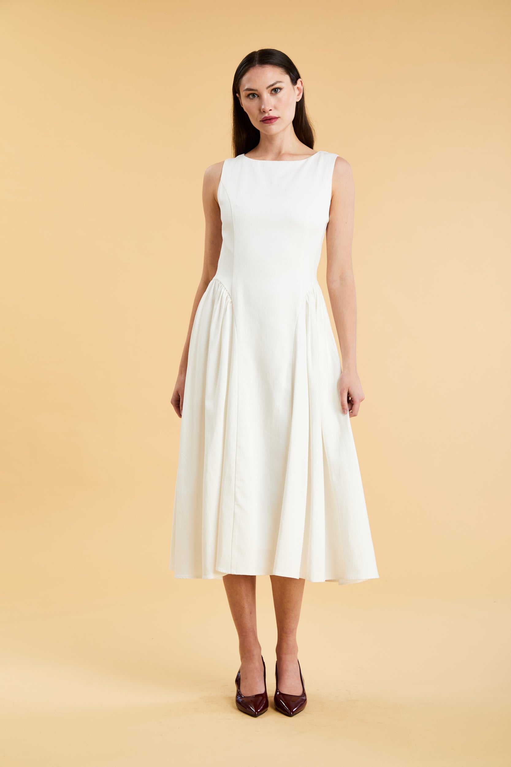 Woman wearing a Triplicity White sleeveless midi dress with gathered side panels on a beige background