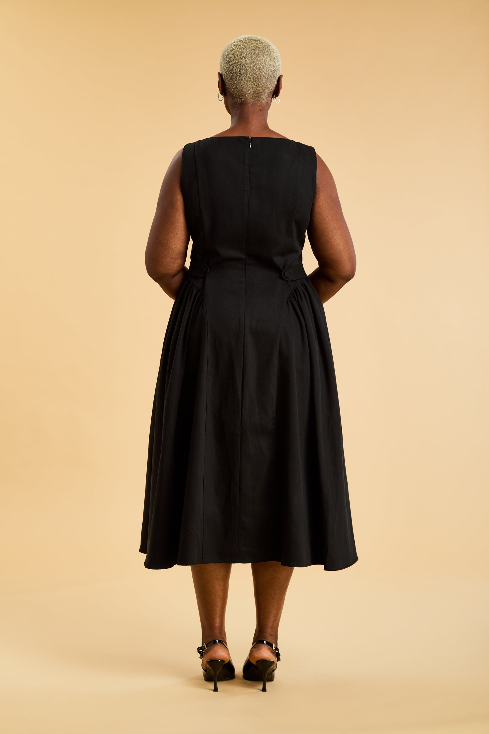 Woman wearing a Triplicity Black sleeveless midi dress with gathered side panels on a beige background