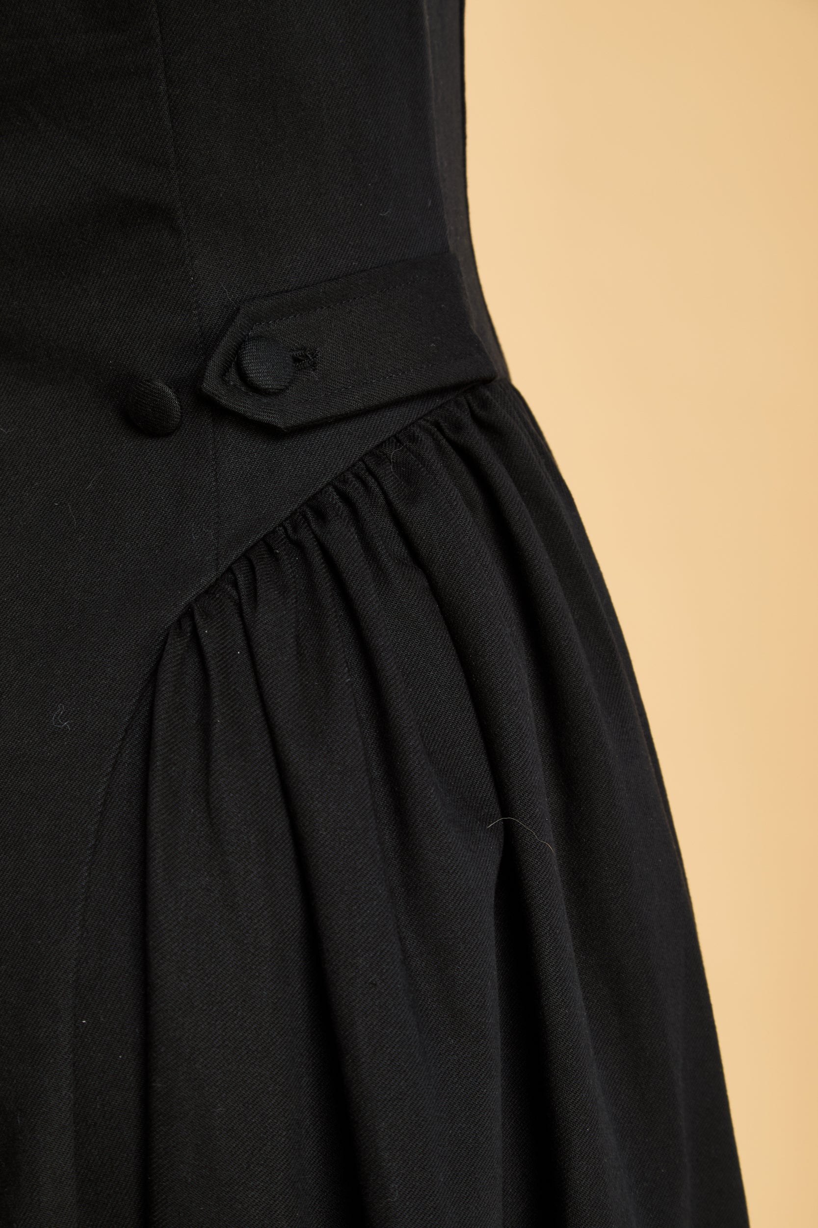 Black dress with an adjustable button detail on a beige background