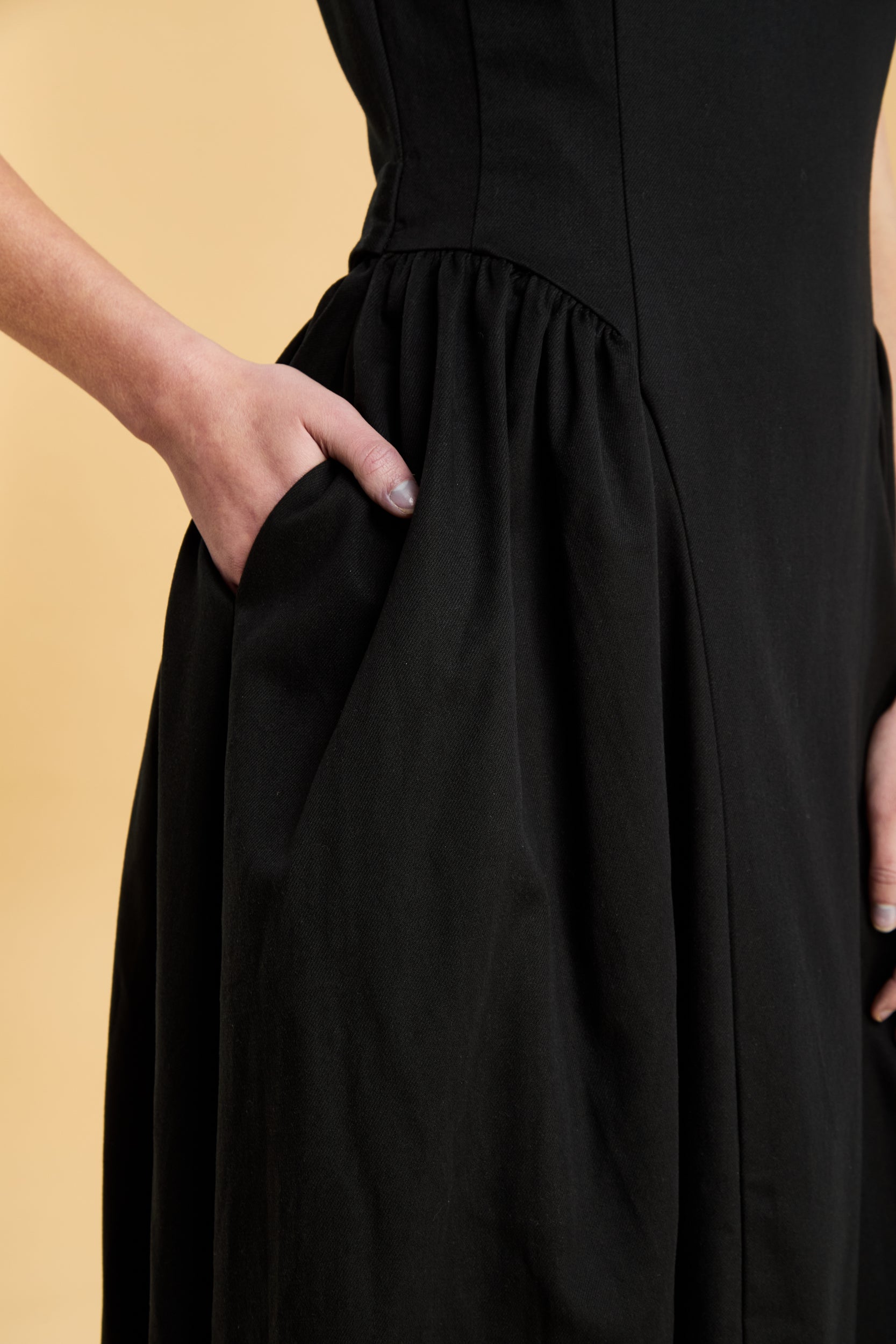 Black dress with a woman's hand in the pocket on a beige background