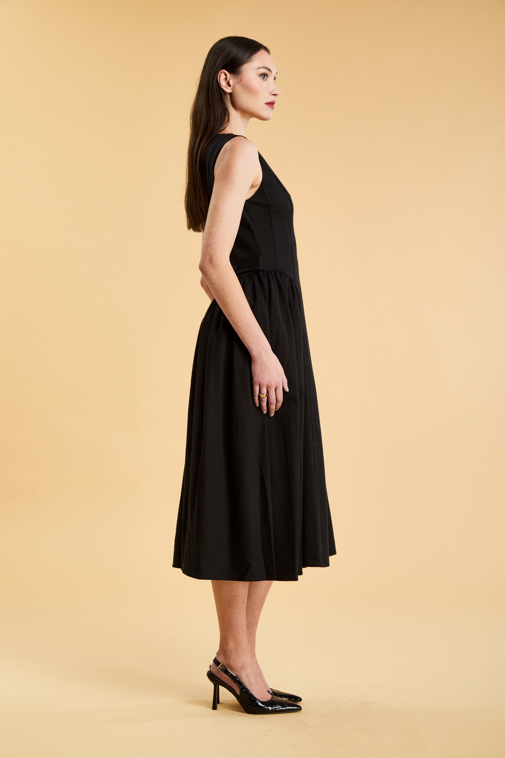 Woman wearing a Triplicity Black sleeveless midi dress with gathered side panels on a beige background