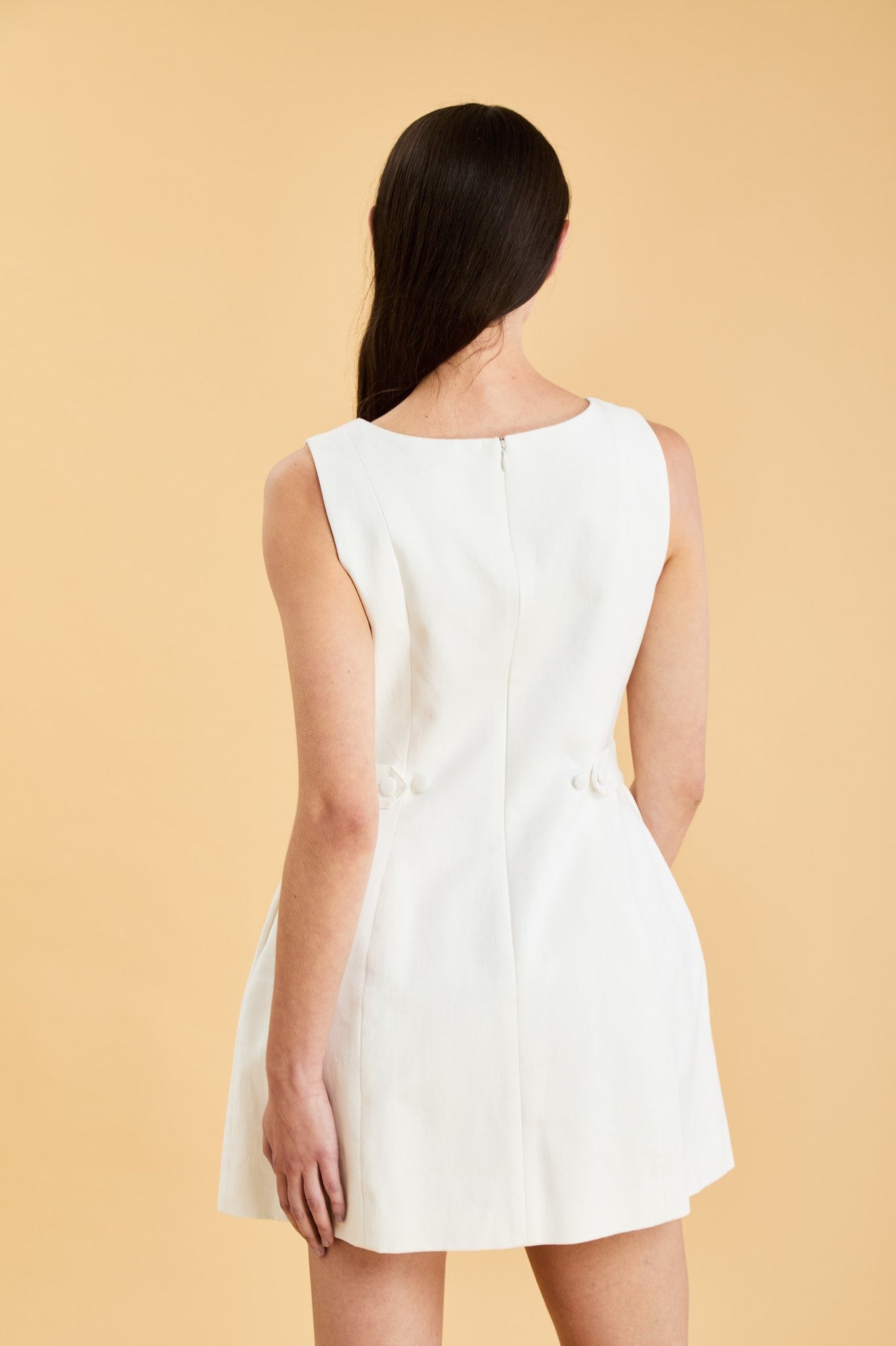 Woman wearing a white sleeveless mini dress against a beige background