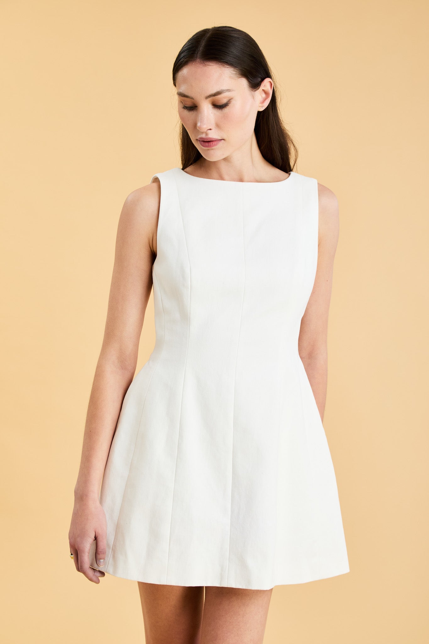Woman wearing a white sleeveless mini dress against a beige background