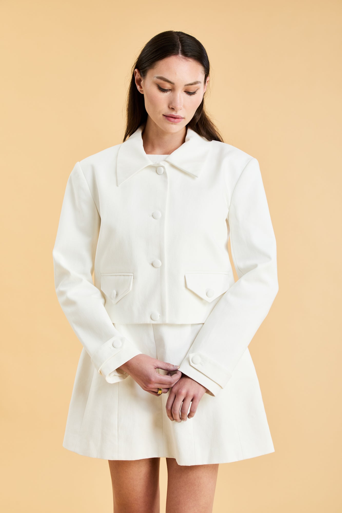 Woman wearing a White Triplicity collared tailored jacket against a beige background front view close up