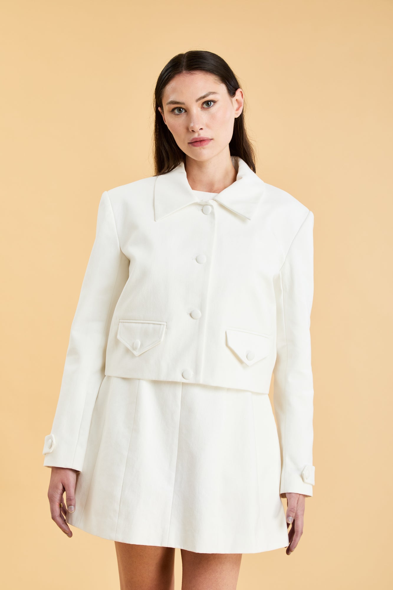 Woman wearing a White Triplicity collared tailored jacket against a beige background front view close up