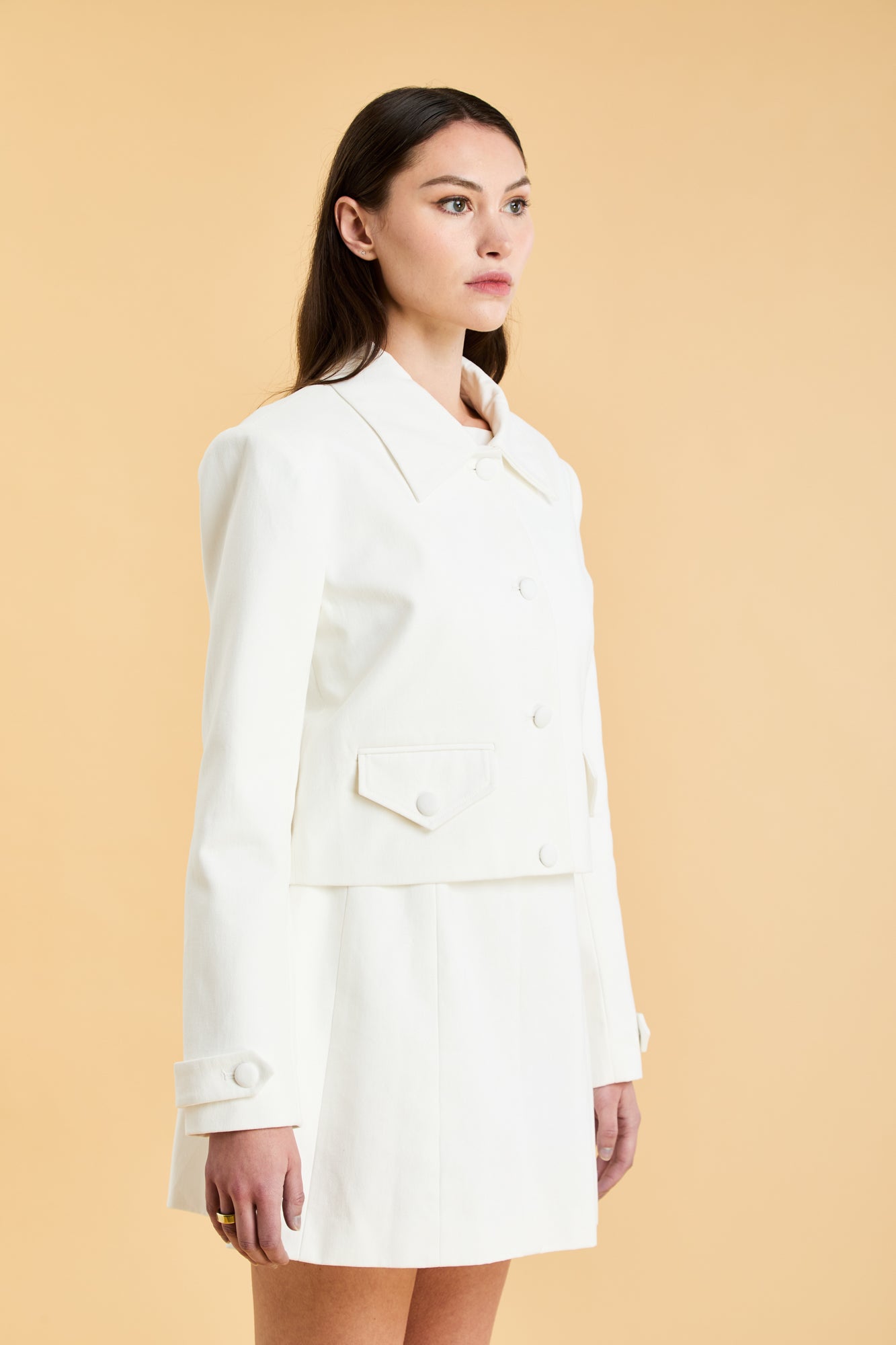 Woman wearing a White Triplicity collared tailored jacket against a beige background front view close up