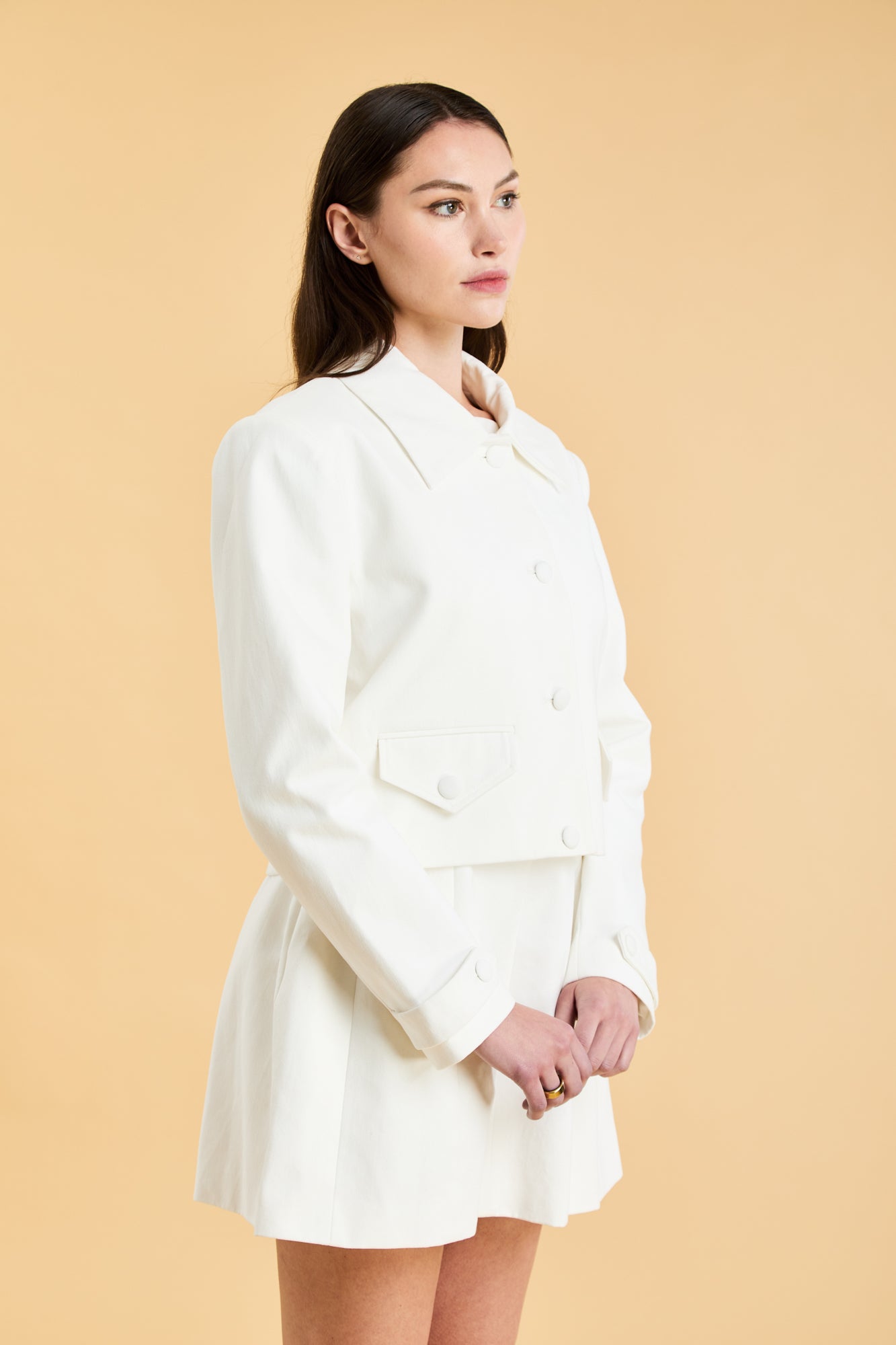 Woman wearing a White Triplicity collared tailored jacket against a beige background front view close up