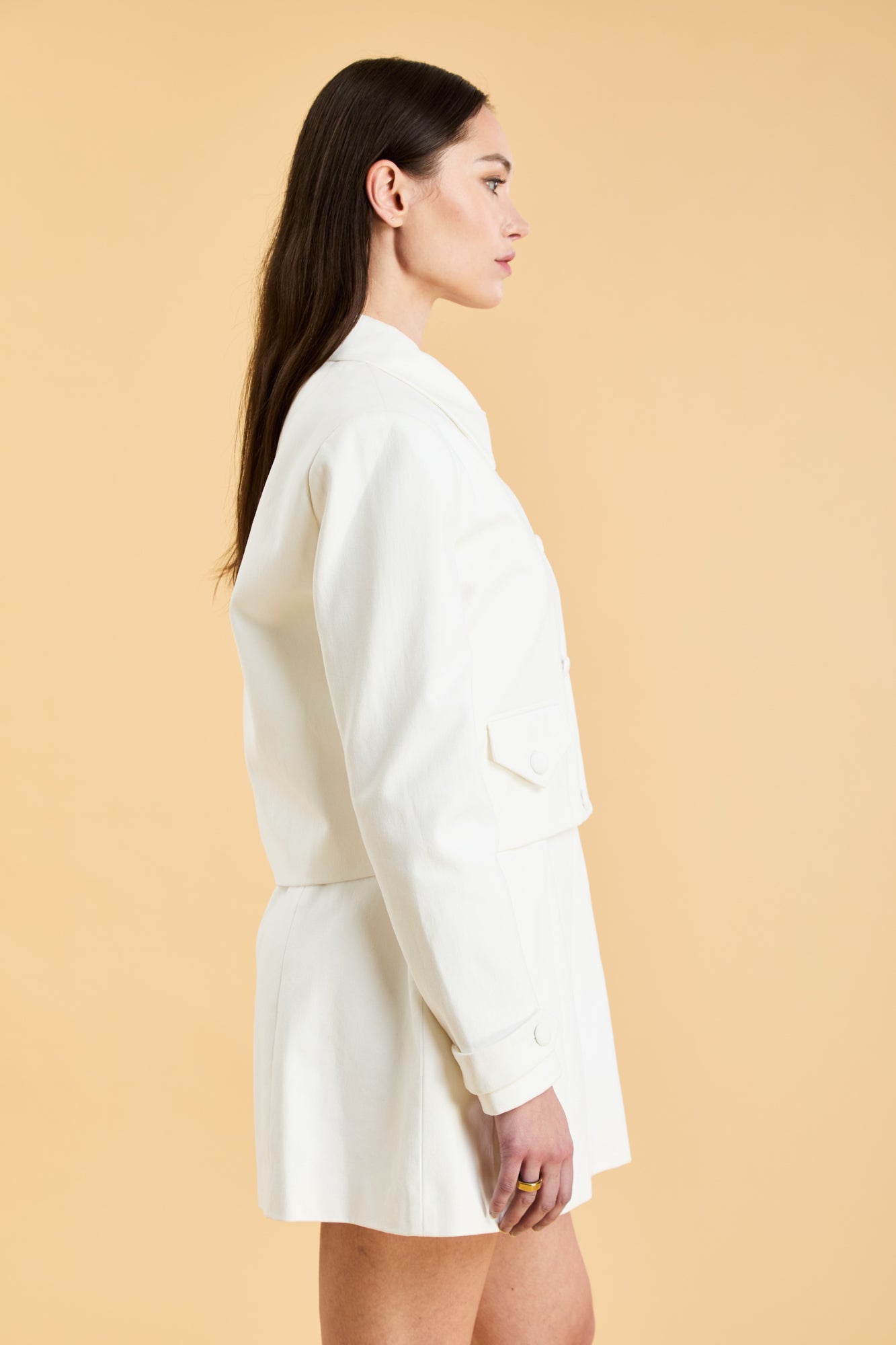 Woman wearing a White Triplicity collared tailored jacket against a beige background side view close up
