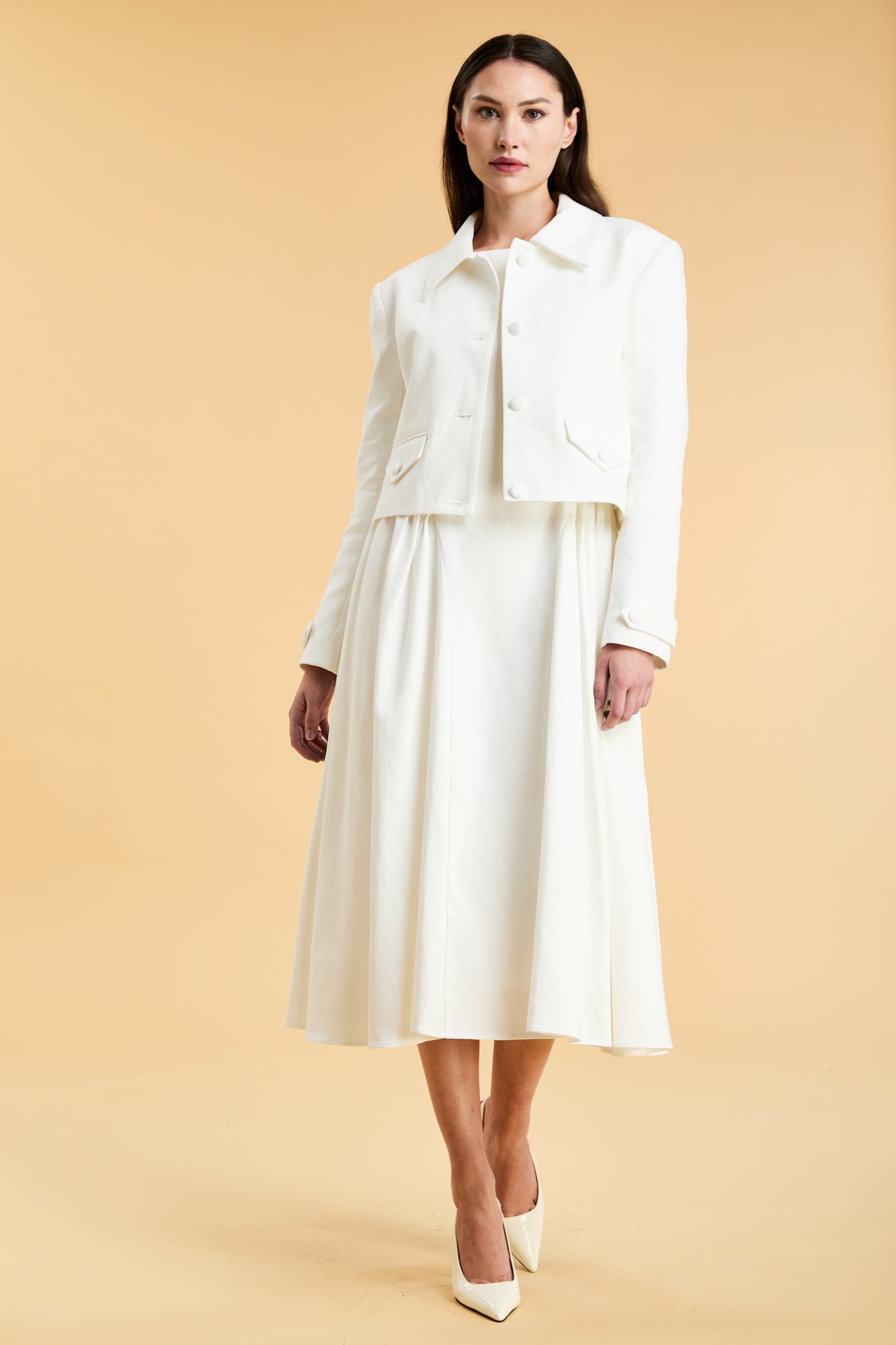 Woman wearing a White Triplicity collared tailored jacket on top of a White Triplicity Eleanor Midi Dress on a beige background front view full body