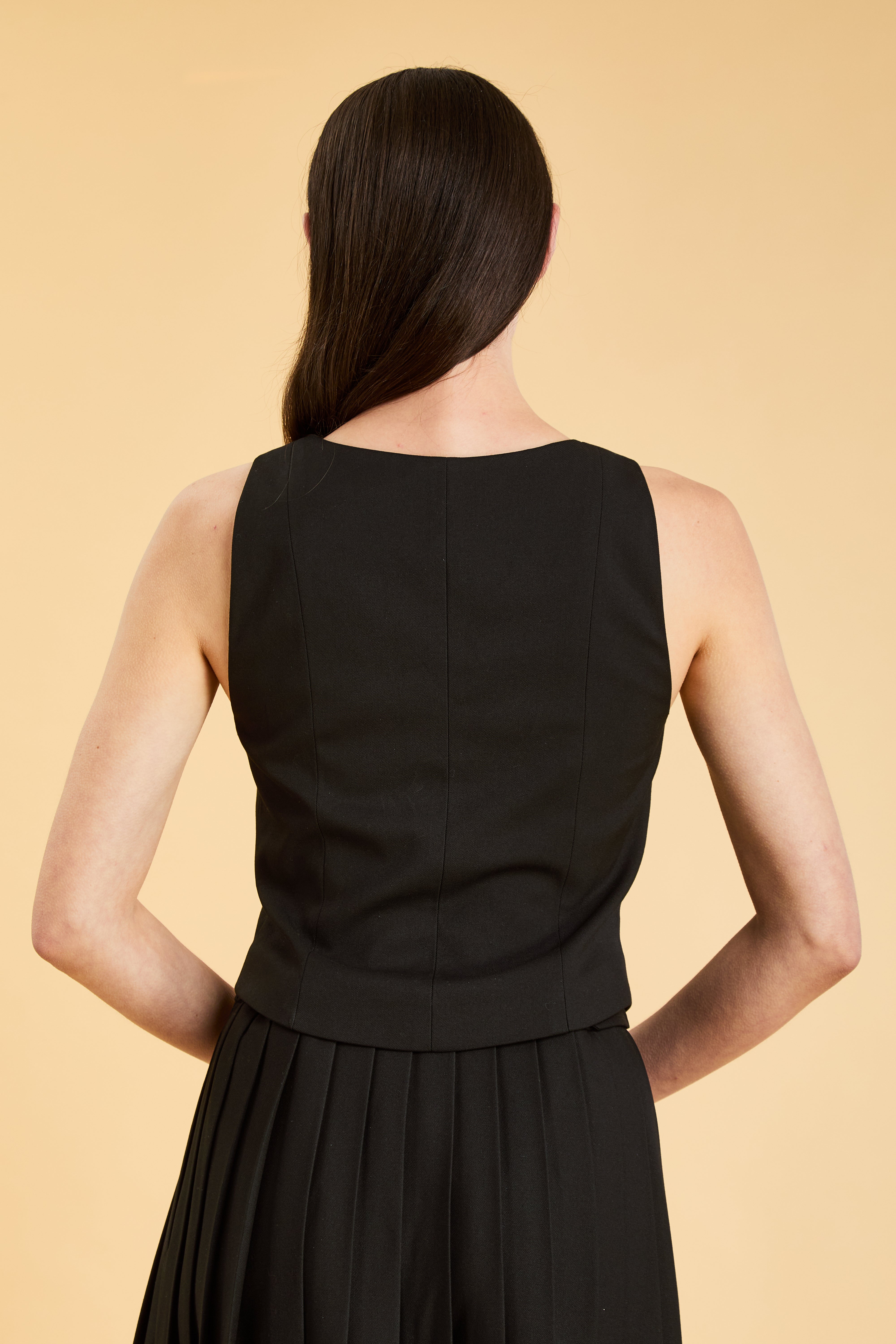 Person wearing a Black Alice double ended zipper Top on a Black pleated Elisabeth Mini skirt against a beige background