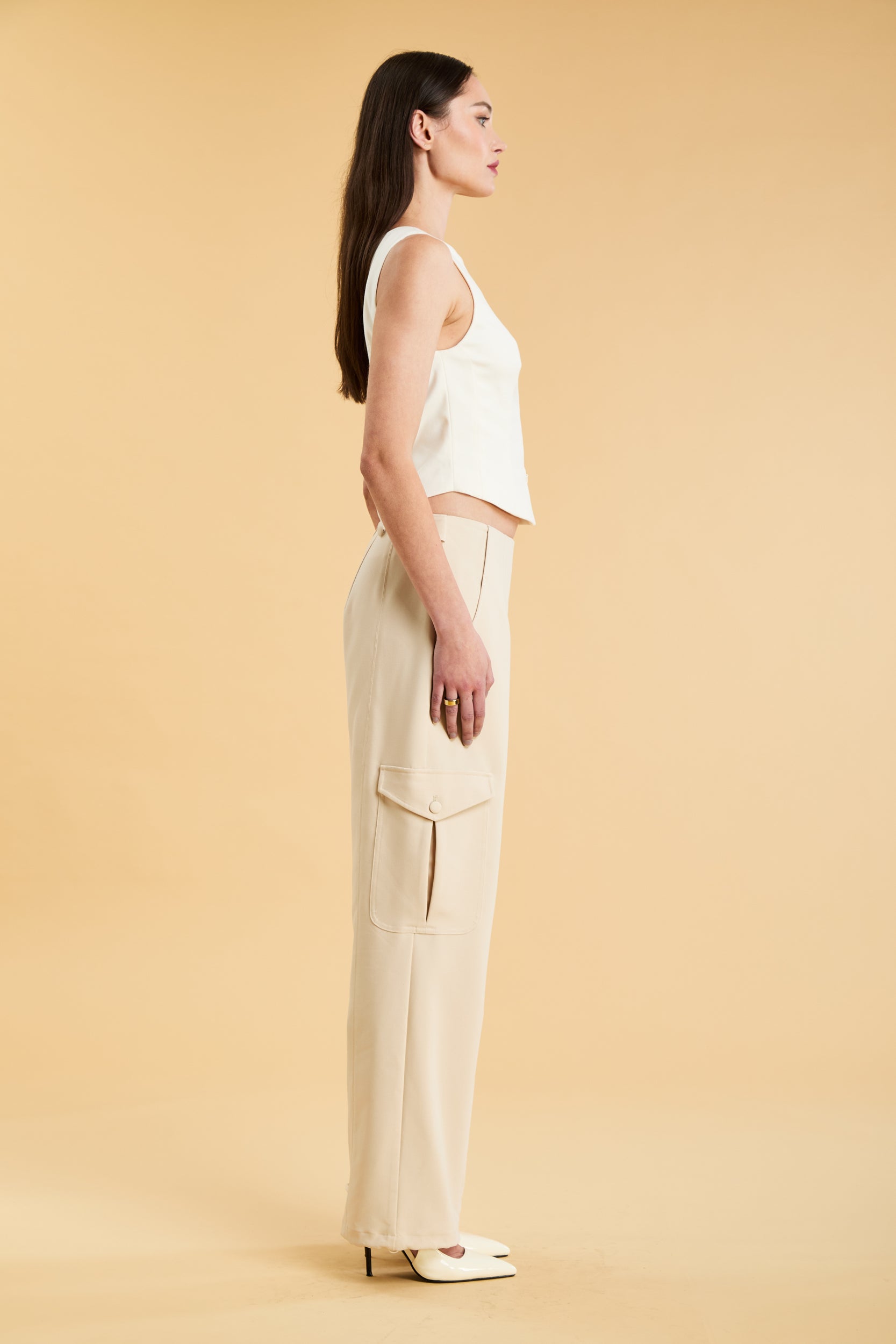 Woman wearing a white sleeveless double zipper top and beige almond Triplicity trousers cargo pants on a beige background