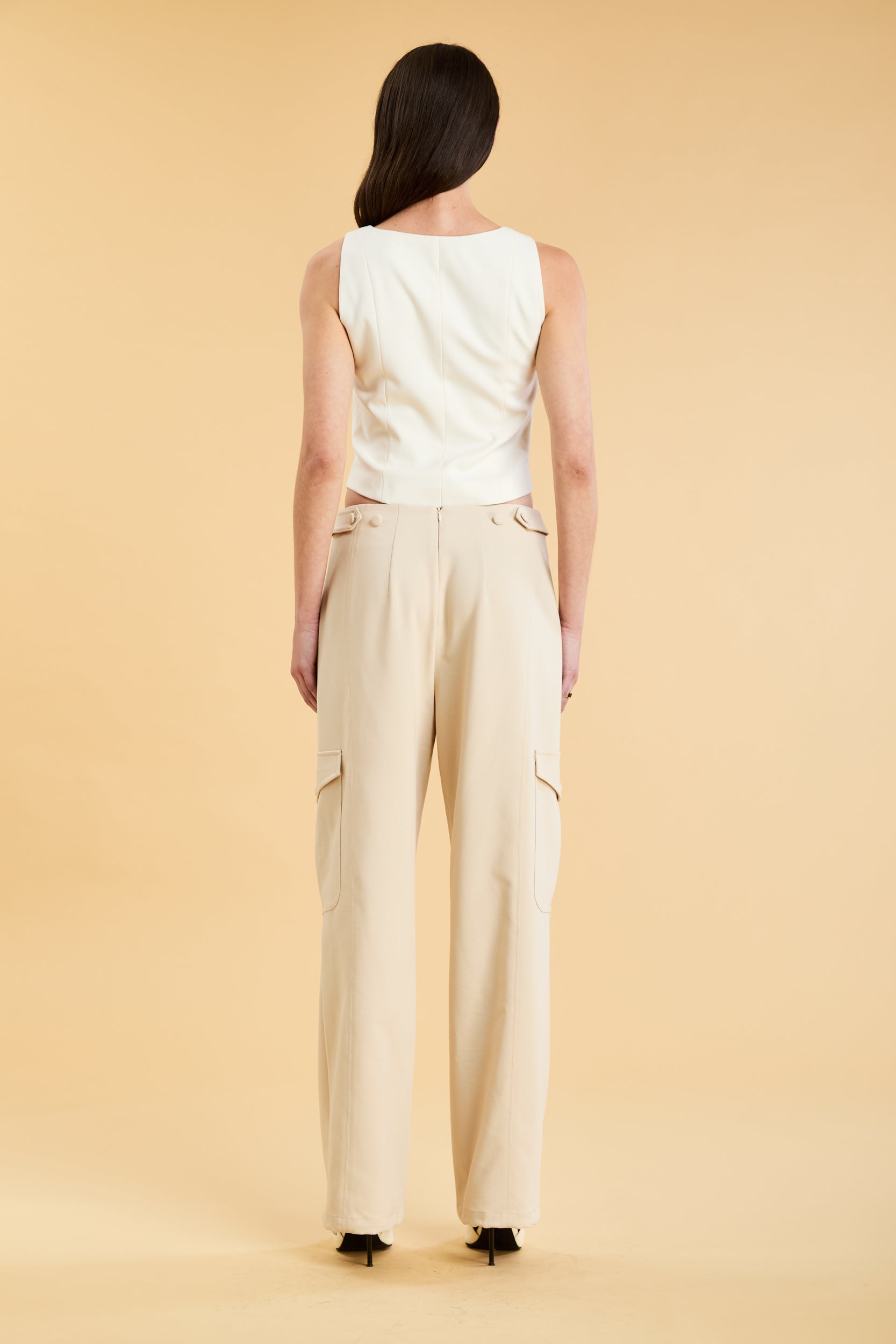 Woman wearing a white sleeveless double zipper top and beige almond Triplicity trousers cargo pants on a beige background